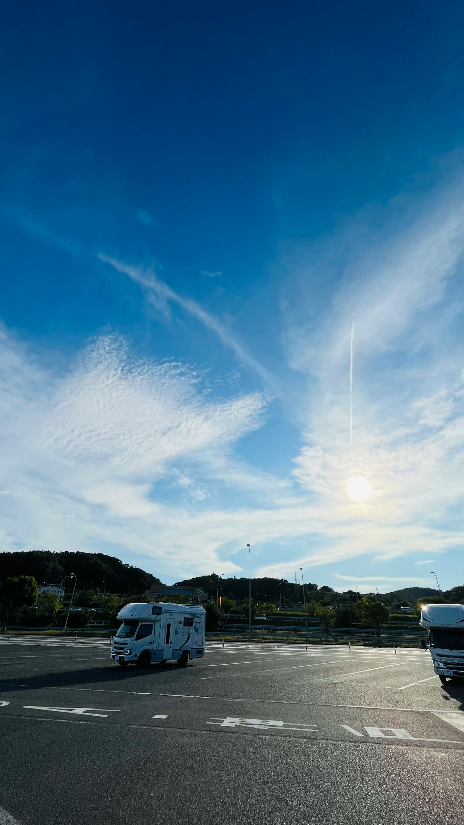 Heller blauer Himmel mit wispy weißen Wolken und einem weißen Wohnmobil rechts