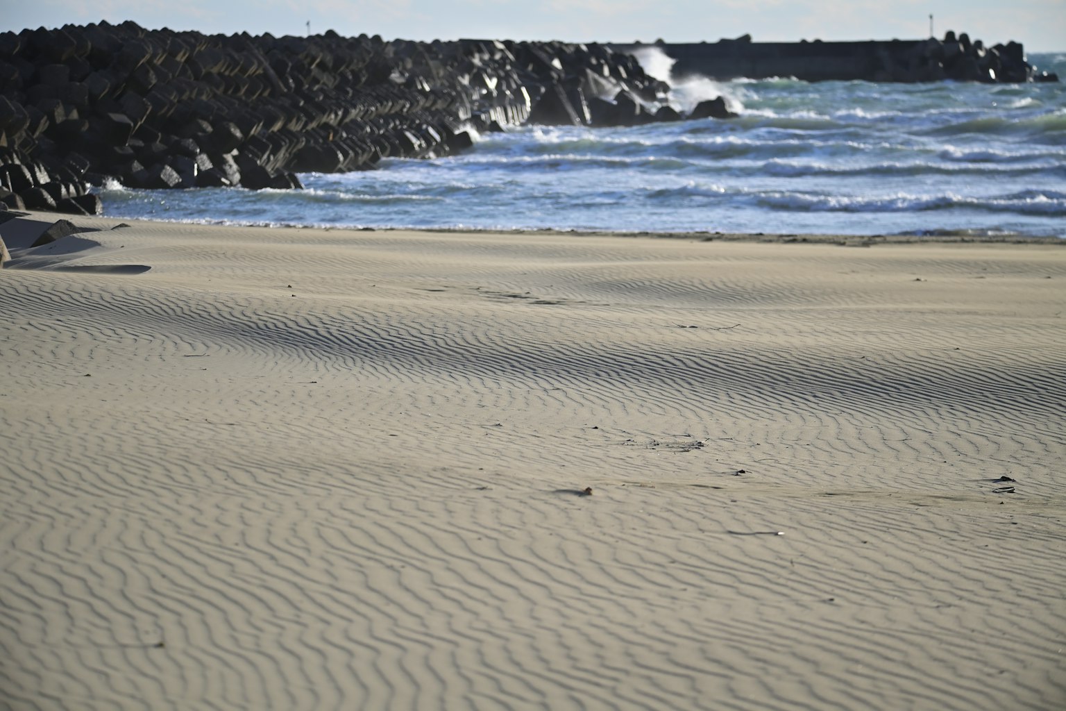 Escena de playa serena con olas rompiendo contra un muelle rocoso y una amplia playa de arena