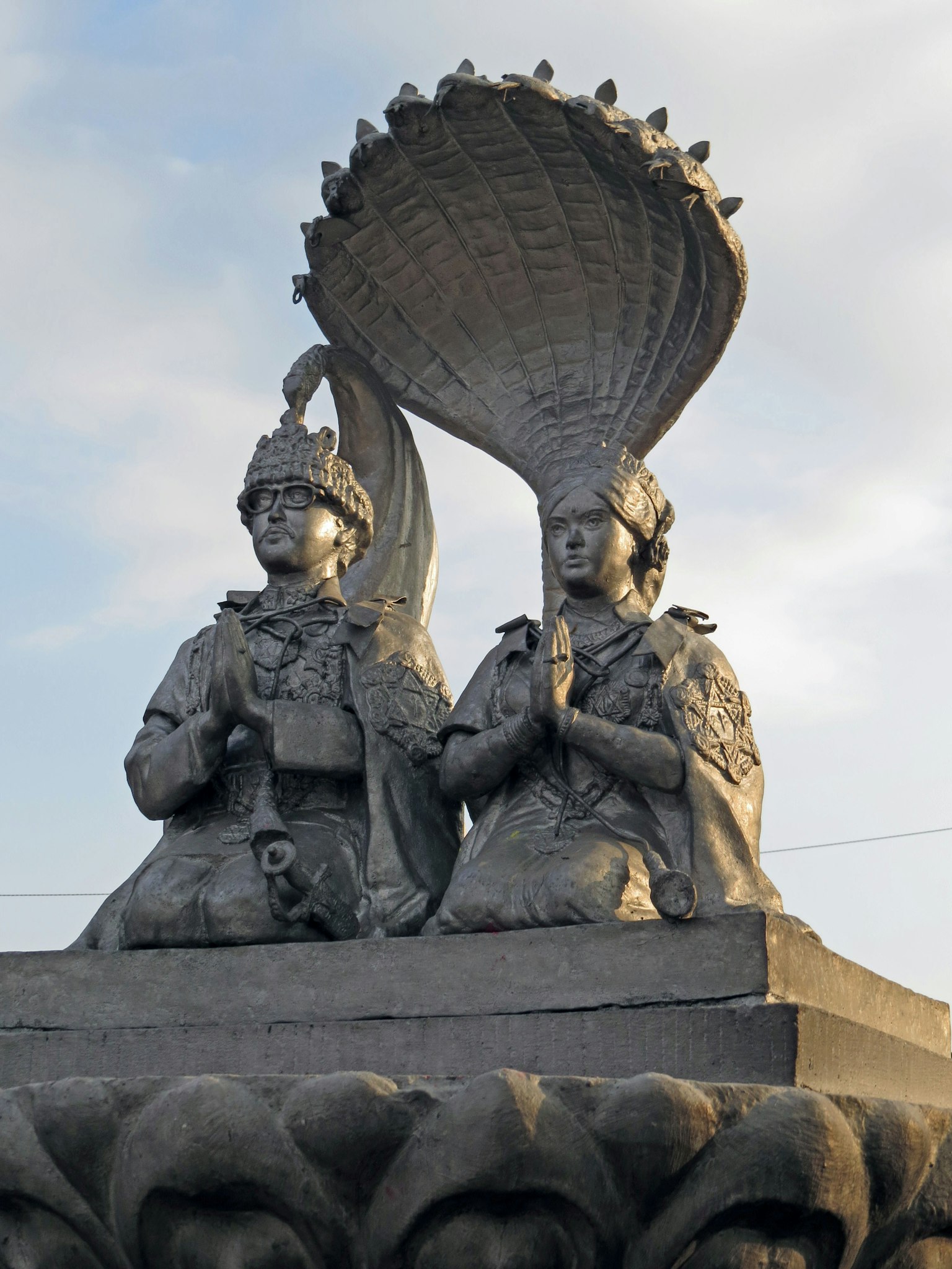 รูปปั้นสองตัวนั่งมือรวมกันและมีพัดตกแต่งขนาดใหญ่ด้านหลัง