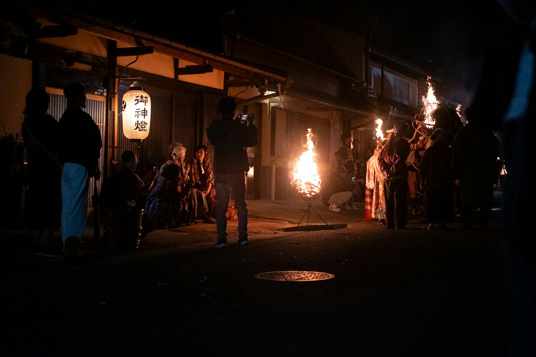 People gathered in a narrow alley at night with lanterns and flames