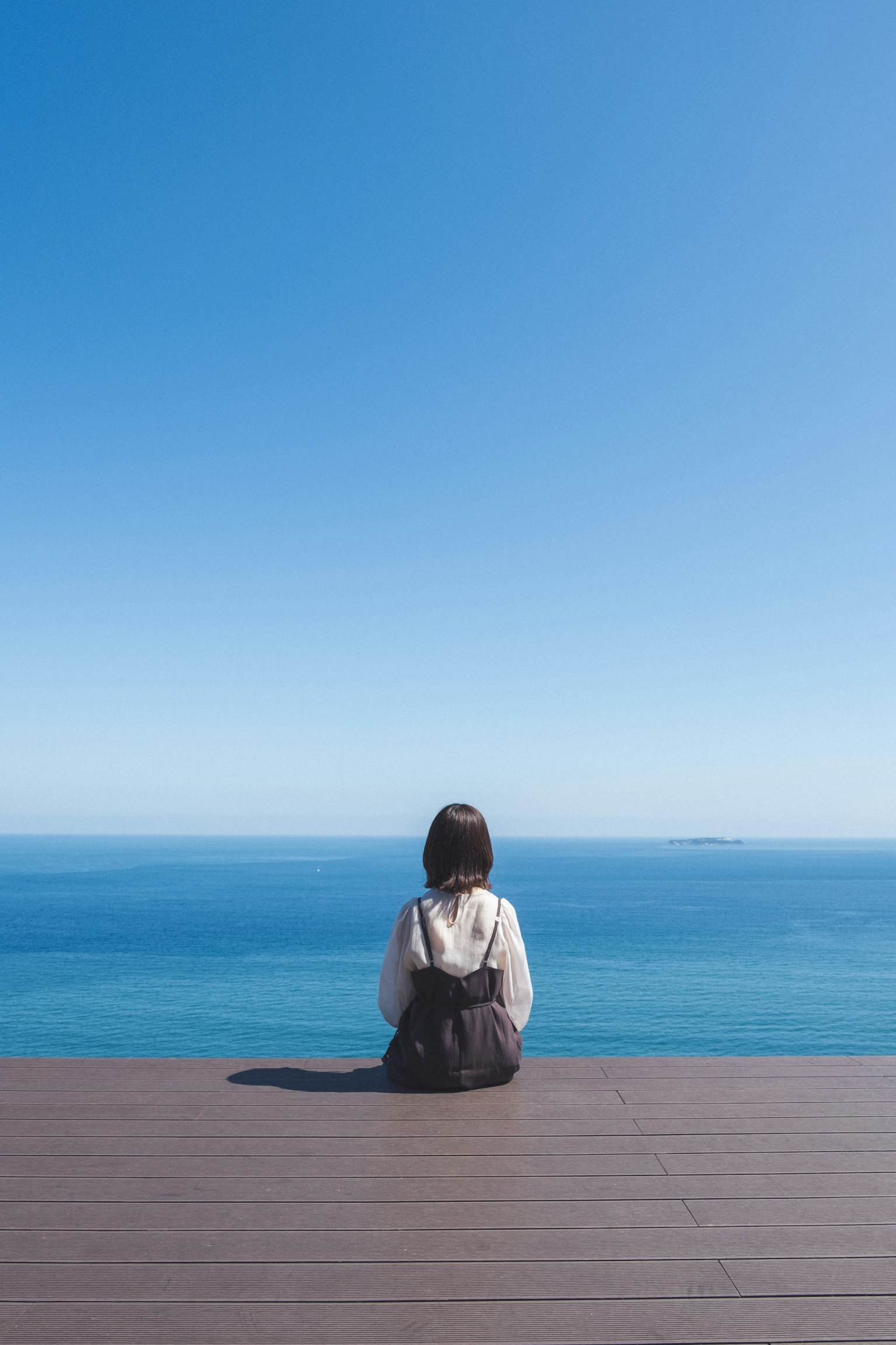 Eine Frau sitzt auf einem Deck und schaut auf den blauen Ozean