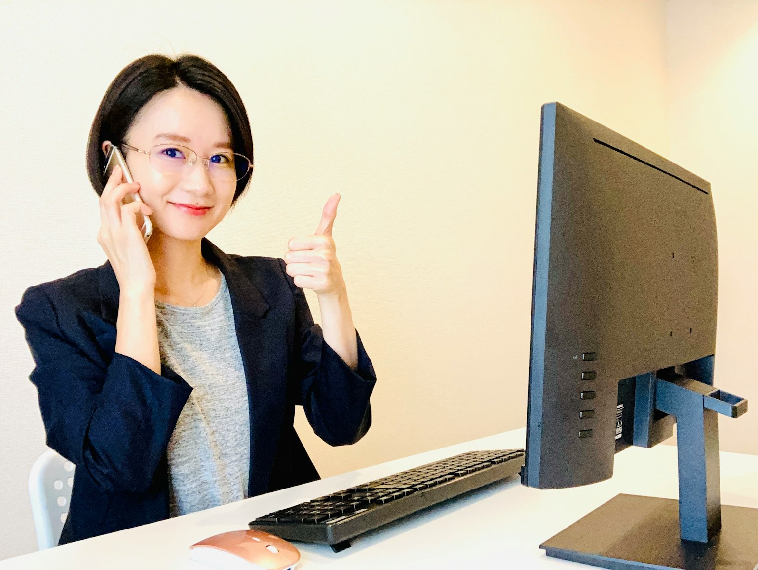 Seorang wanita duduk di depan komputer memberikan jempol sambil berbicara di telepon