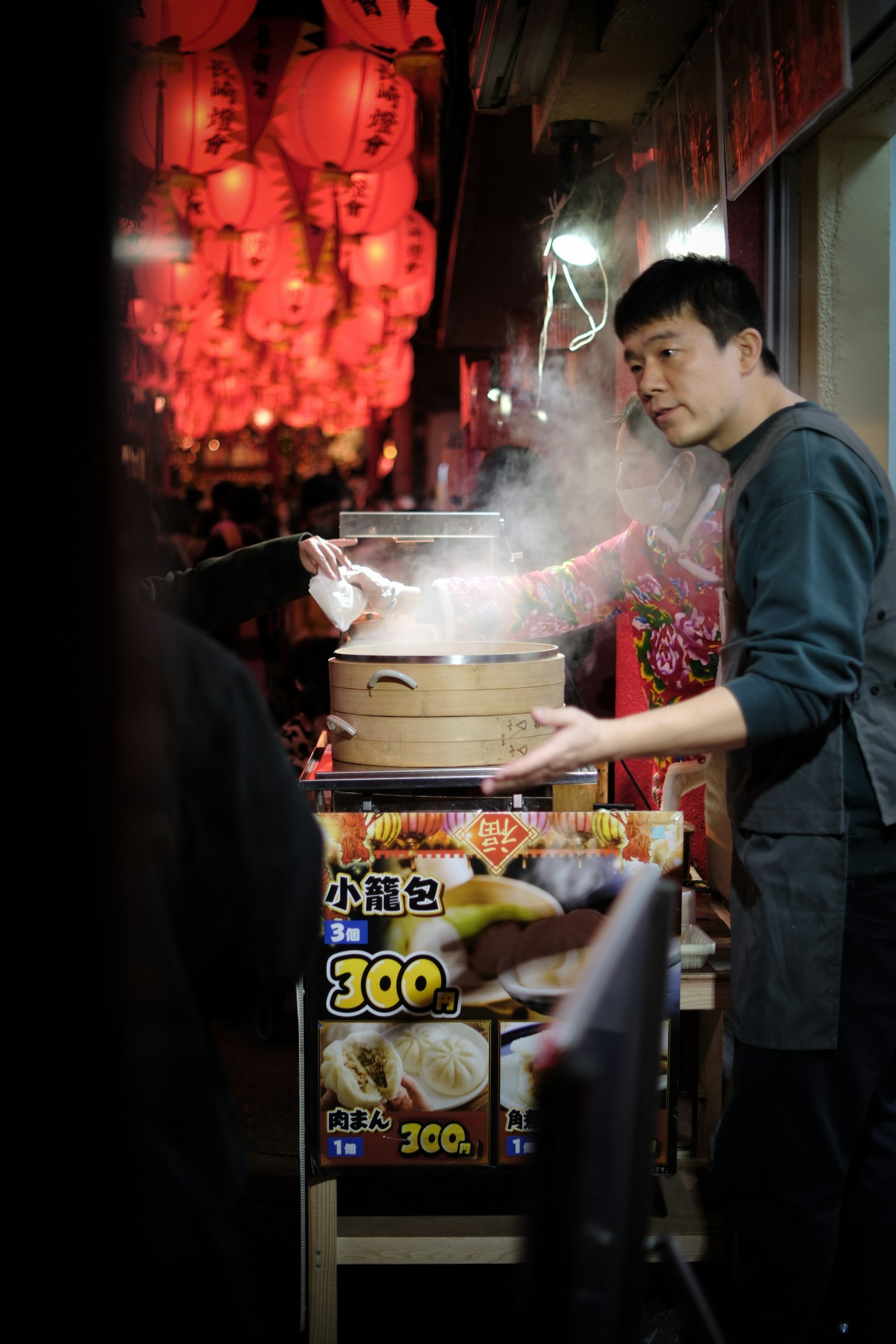 夜市小贩手持蒸锅，周围装饰着红色灯笼