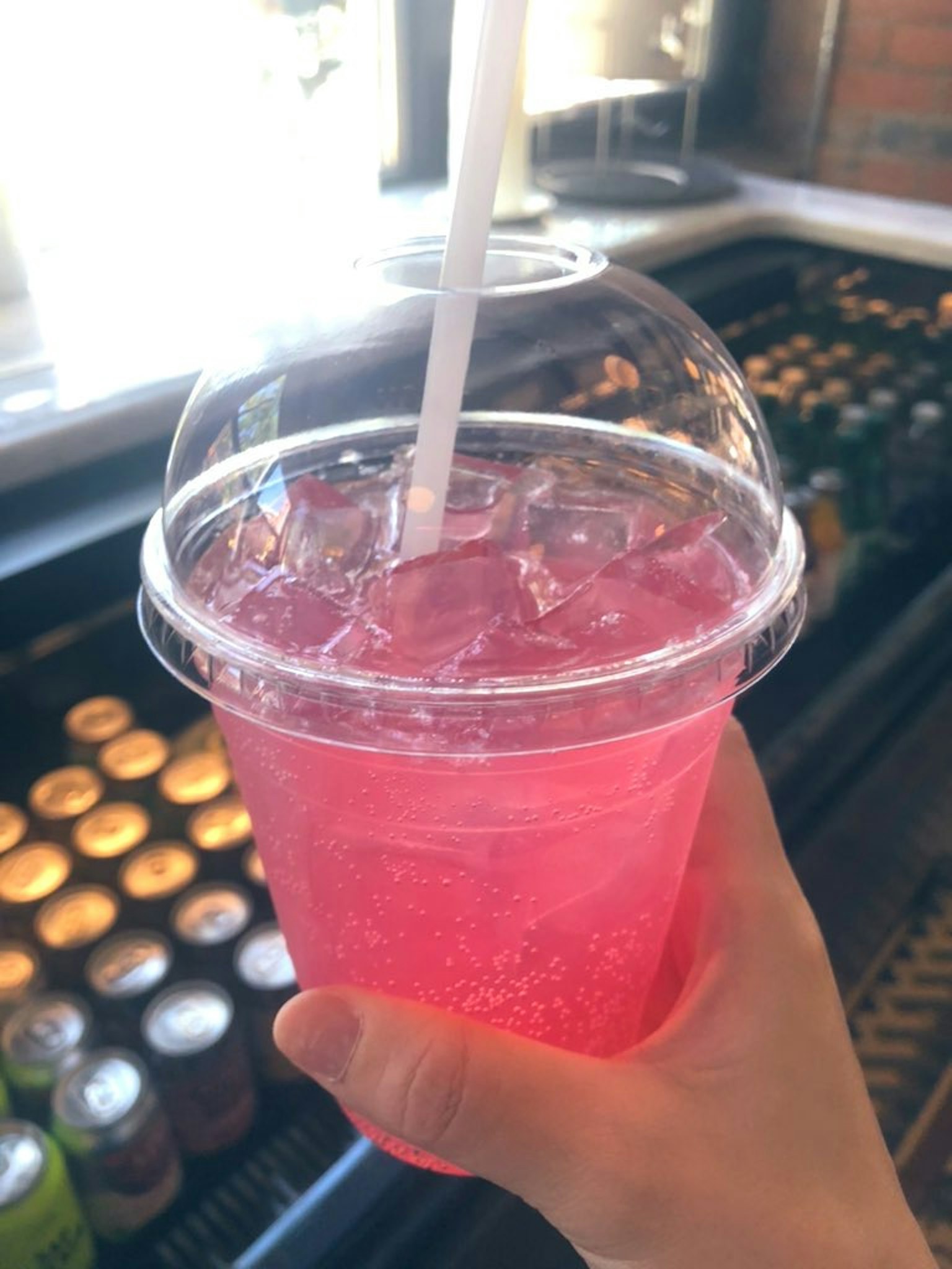 Una persona sosteniendo un vaso transparente de bebida espumosa rosa