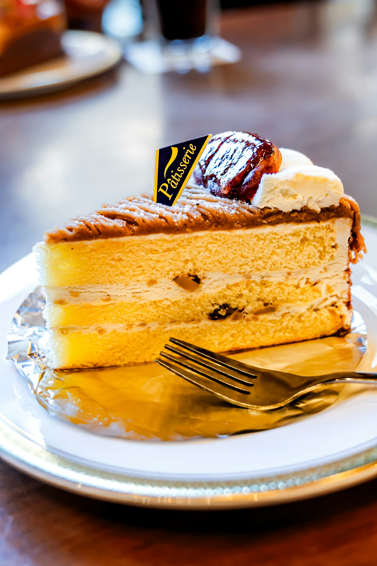 美味しそうなケーキのスライスが白い皿に置かれている フォークが横に置かれ ケーキにはクリームとトッピングがある