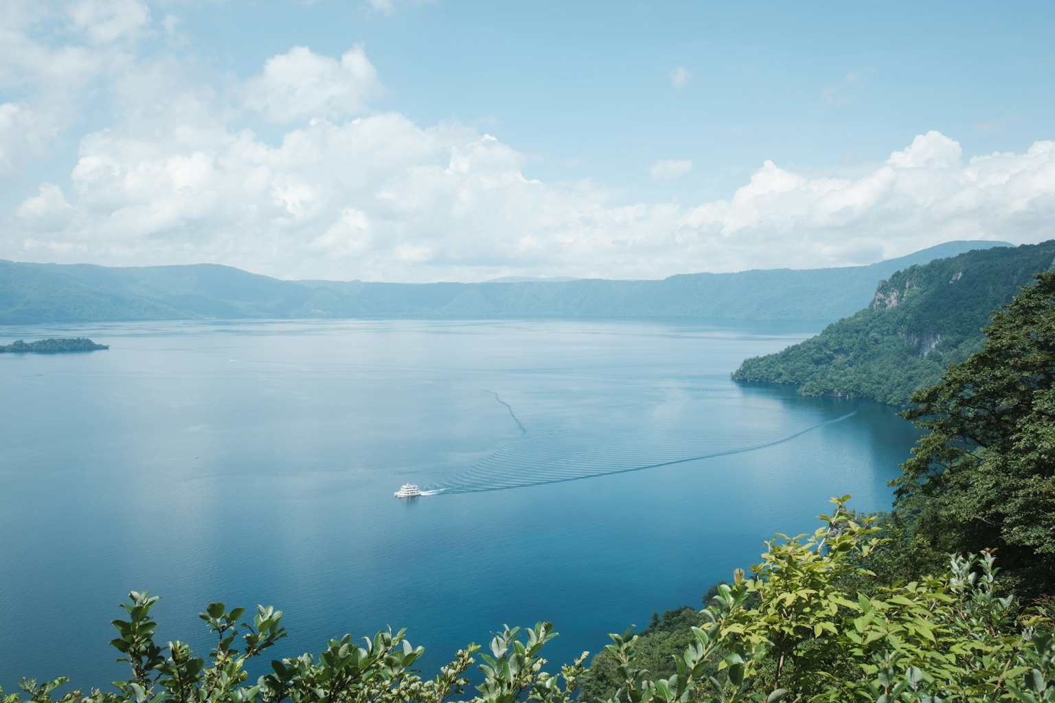 Un lago azul sereno rodeado de colinas verdes y montañas distantes