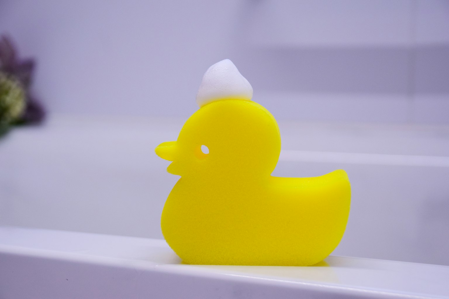 Esponja en forma de pato amarillo en el borde de una bañera