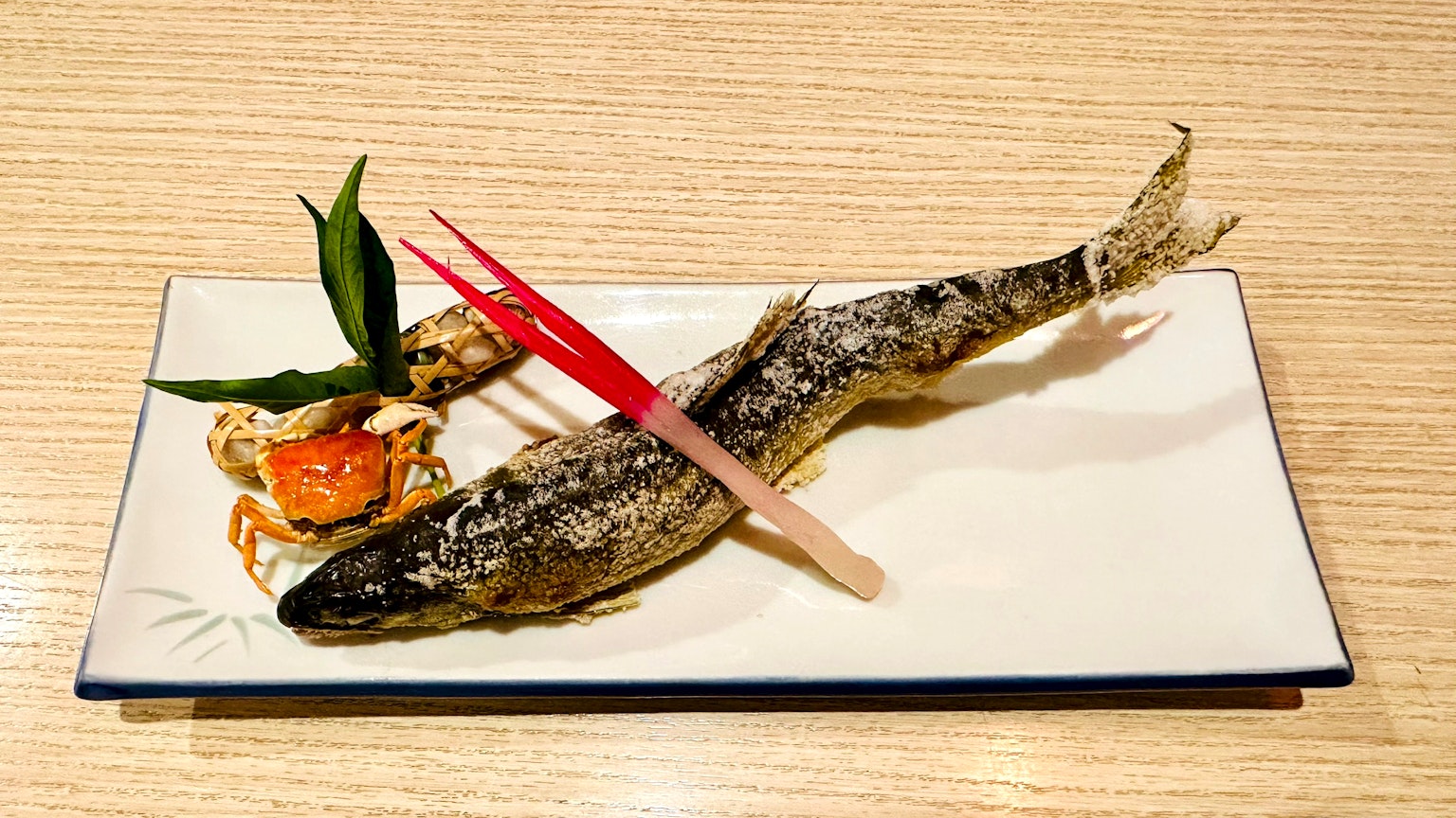 Pesce alla griglia su un piatto con un piccolo antipasto e foglie decorative