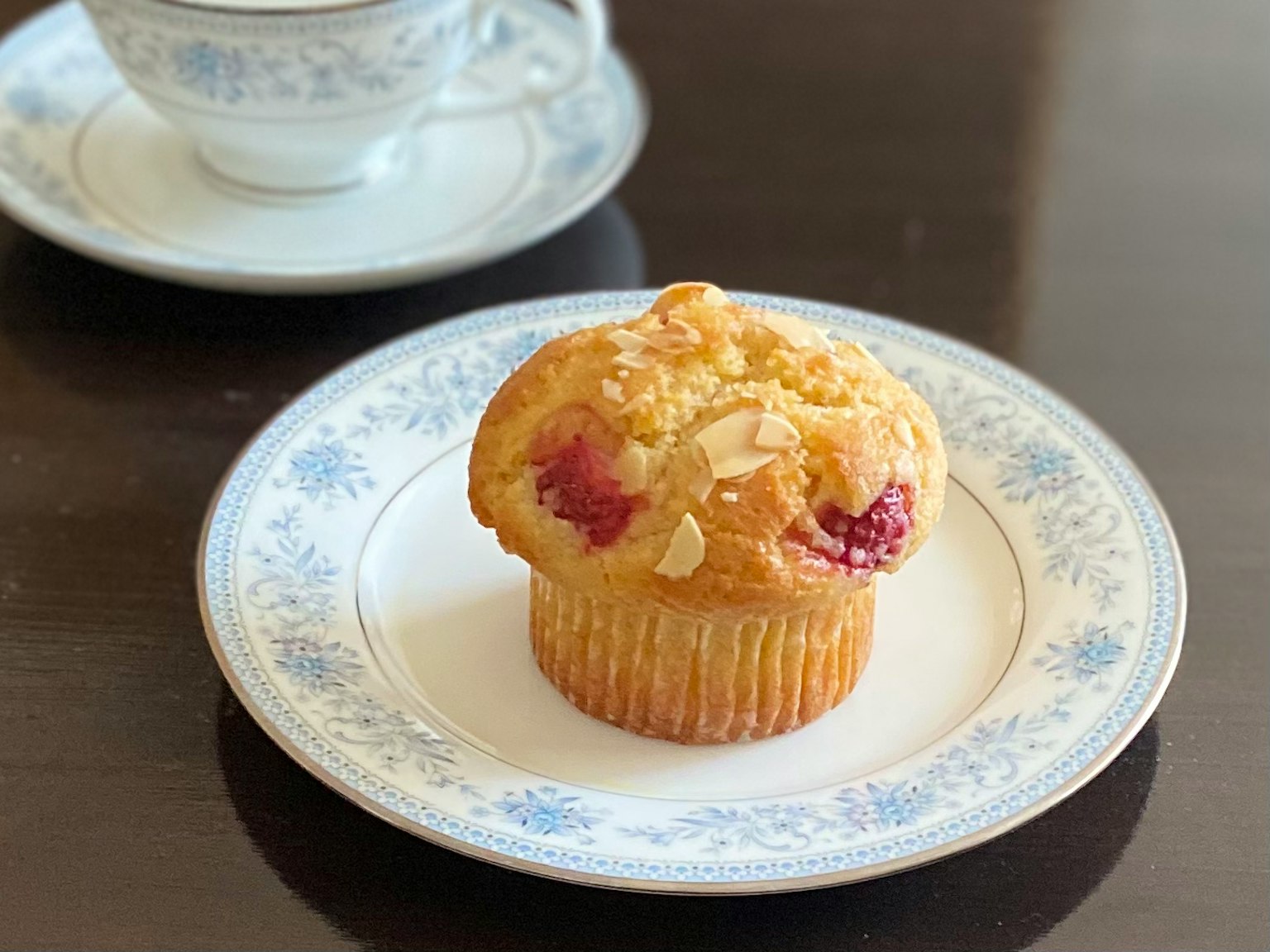 Muffin de frambuesa y almendra en un plato decorativo con una taza de té al fondo