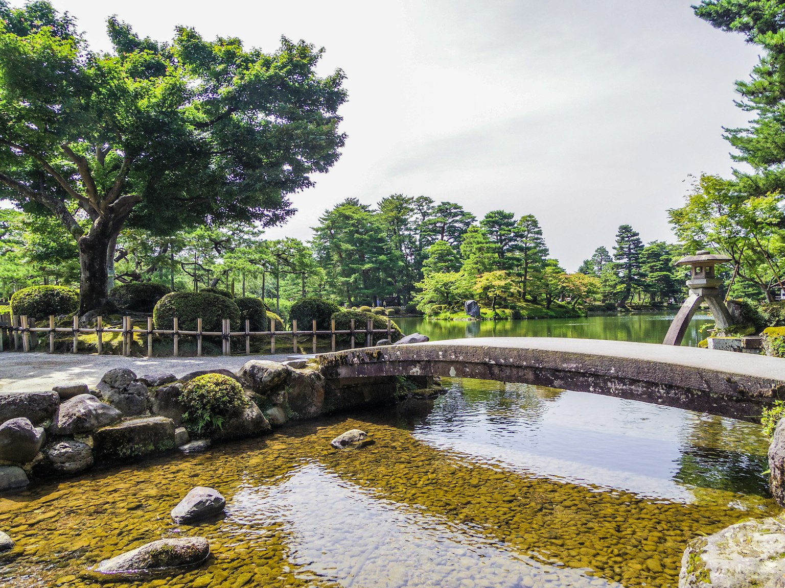 Vista panoramica di un bellissimo giardino con un ponte e uno stagno circondato da alberi verdi e cielo blu