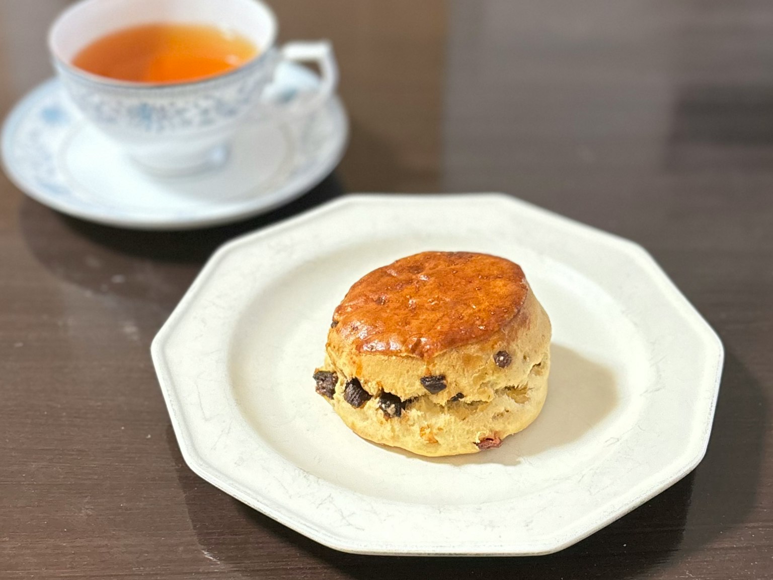 Uno scone alle gocce di cioccolato su un piatto decorativo con una tazza di tè sullo sfondo