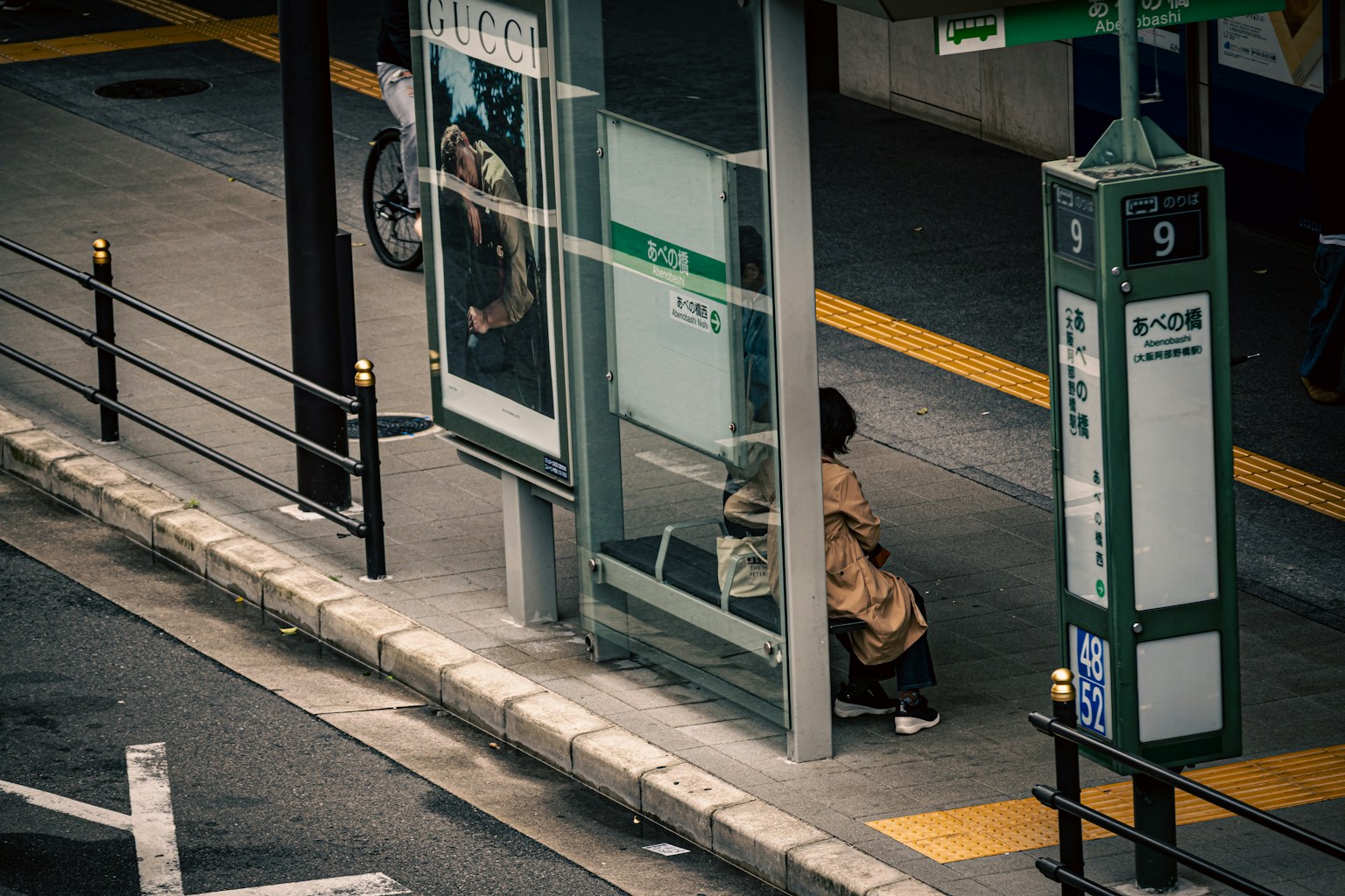 Seseorang duduk di halte bus dengan pemandangan kota di latar belakang