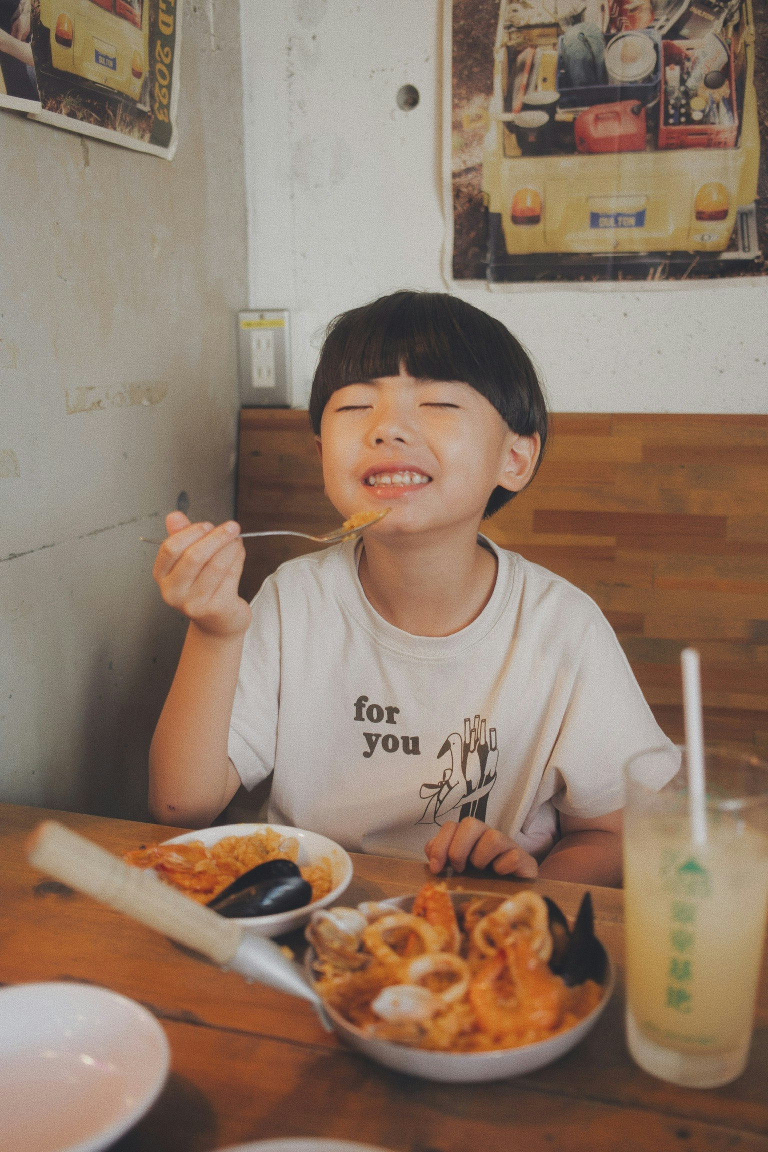 เด็กยิ้มขณะเพลิดเพลินกับมื้ออาหารที่มีจานและเครื่องดื่มบนโต๊ะ