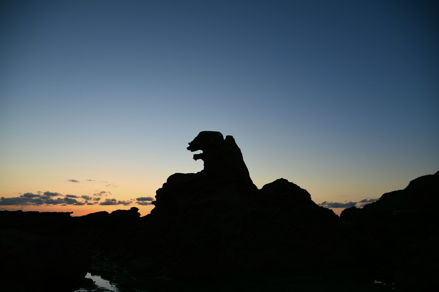 Silhouette eines Felsens, der einem Löwen ähnelt, vor einem Dämmerungshimmel