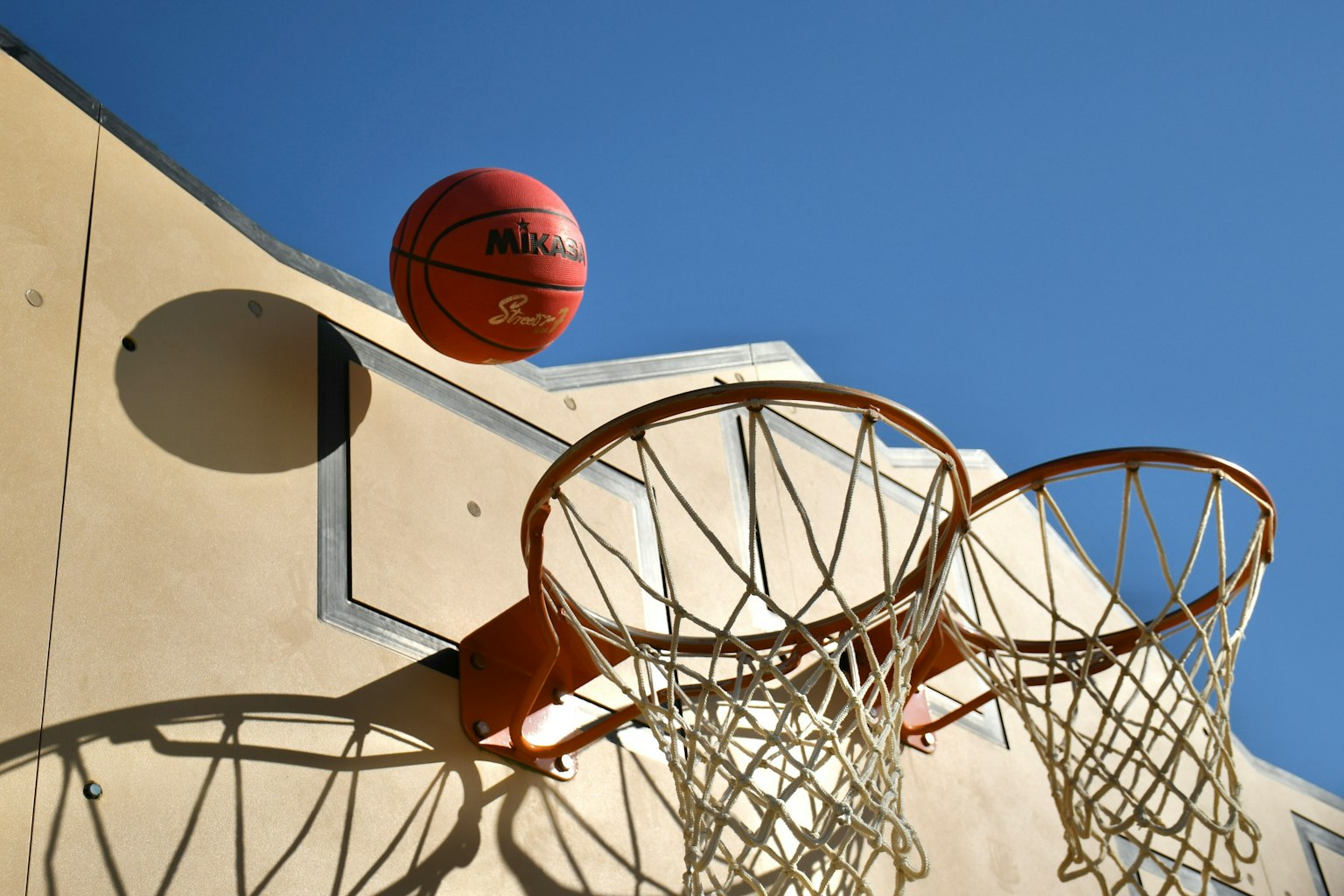 Un pallone da basket in aria sopra due canestri contro un cielo blu chiaro