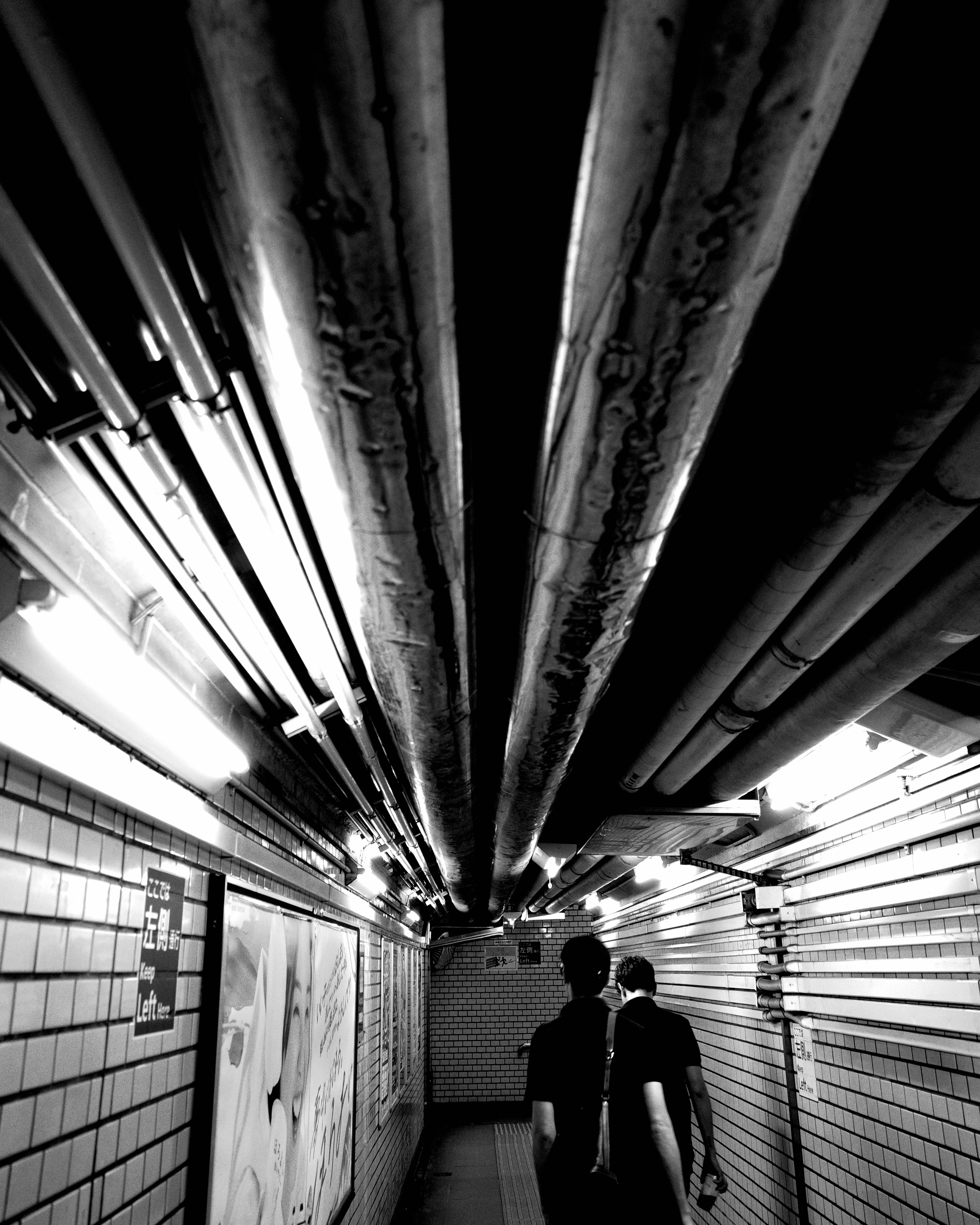 couloir souterrain éclairé par des néons et deux silhouettes