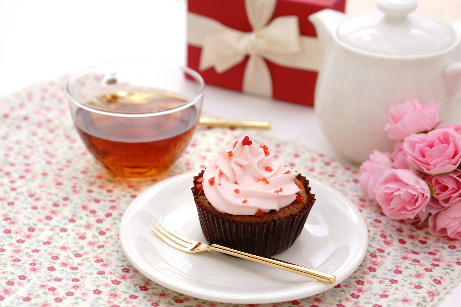 Hadiah dengan pita merah, teh, cupcake dengan frosting pink dan mawar pink