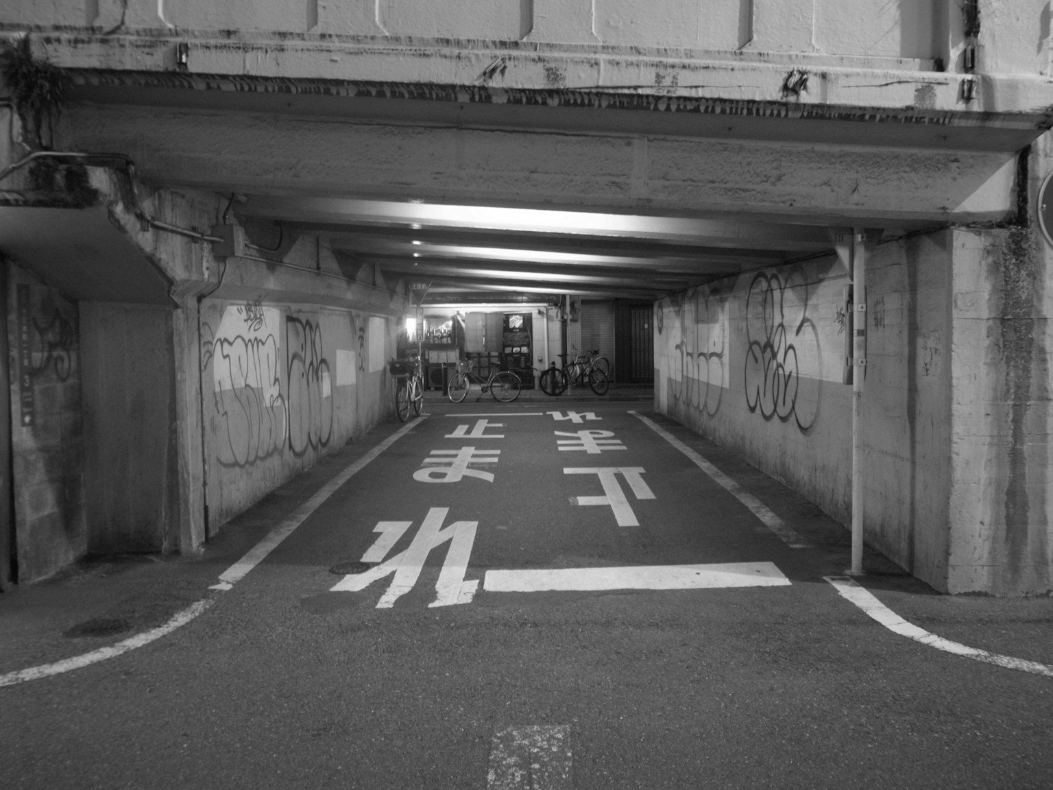 一个昏暗的地下通道，墙上有白色路标和涂鸦