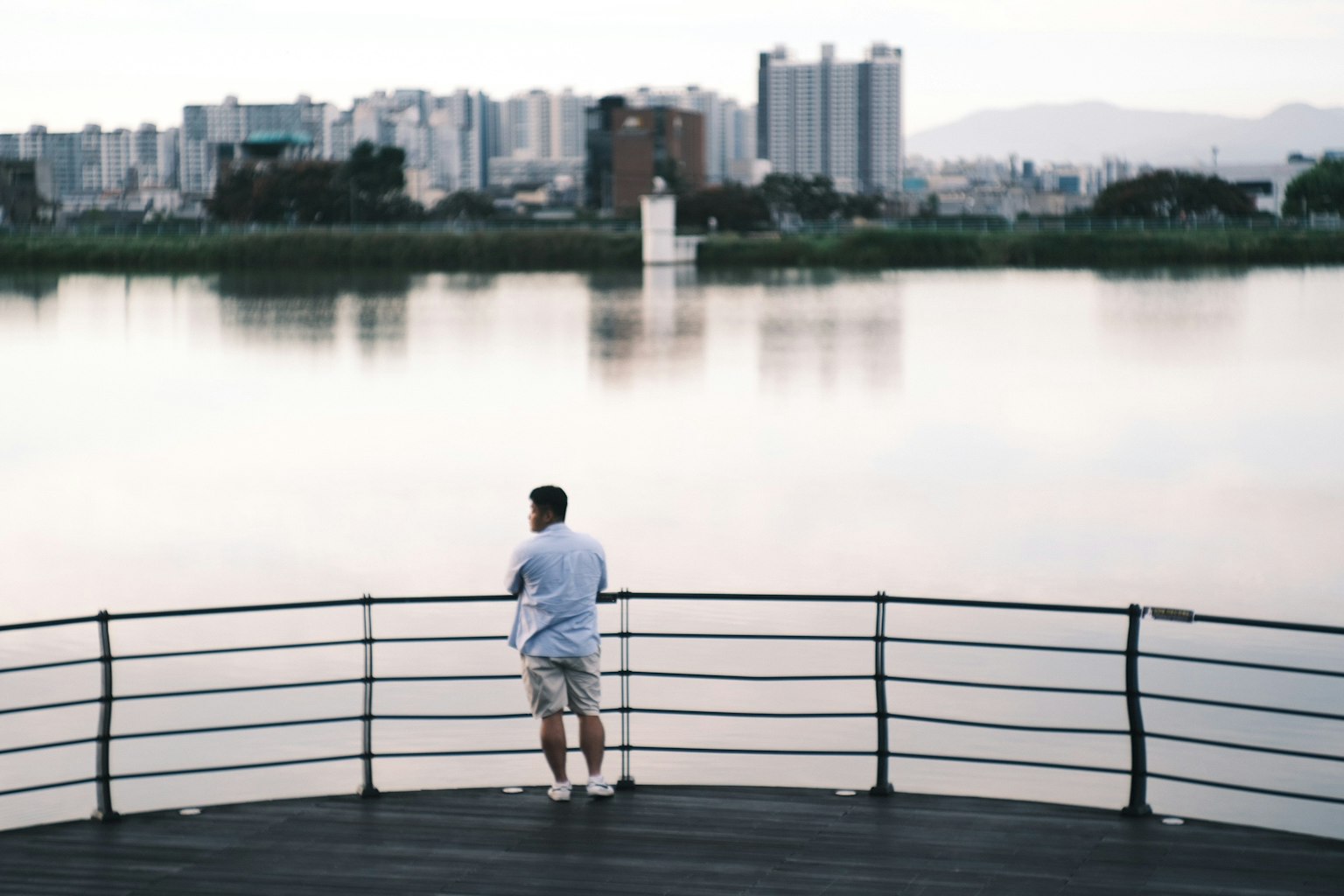 湖のほとりで考え込む男性と都市の背景