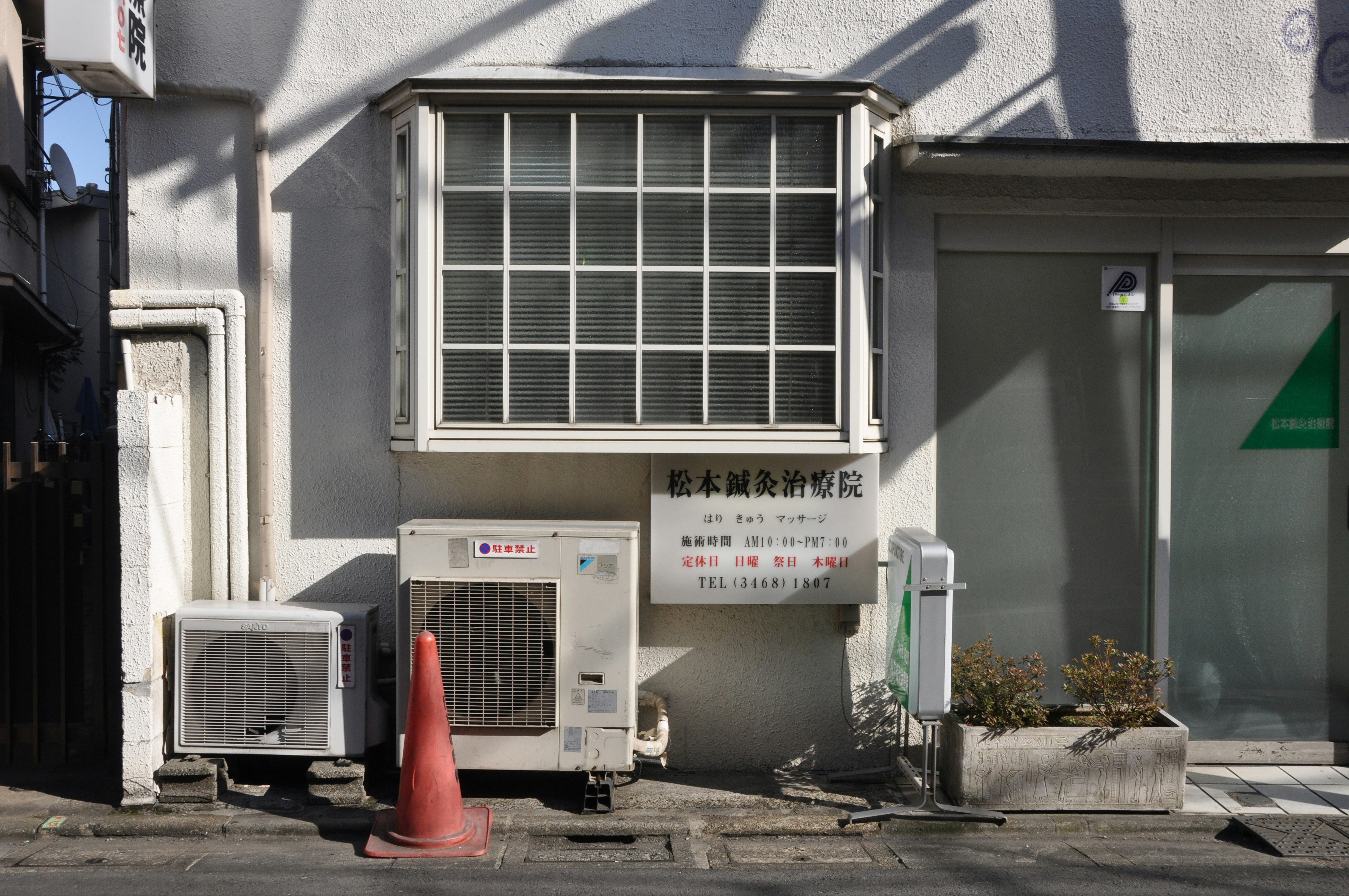 路地の壁に並ぶ空調機器と配管のある建物外観