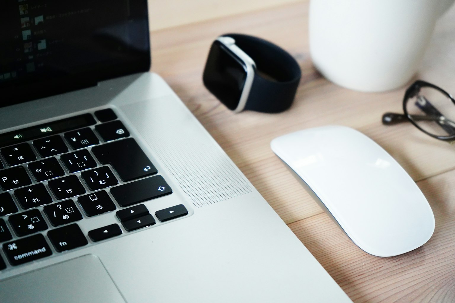 Un laptop, un mouse, uno smartwatch, occhiali e una tazza bianca su una scrivania