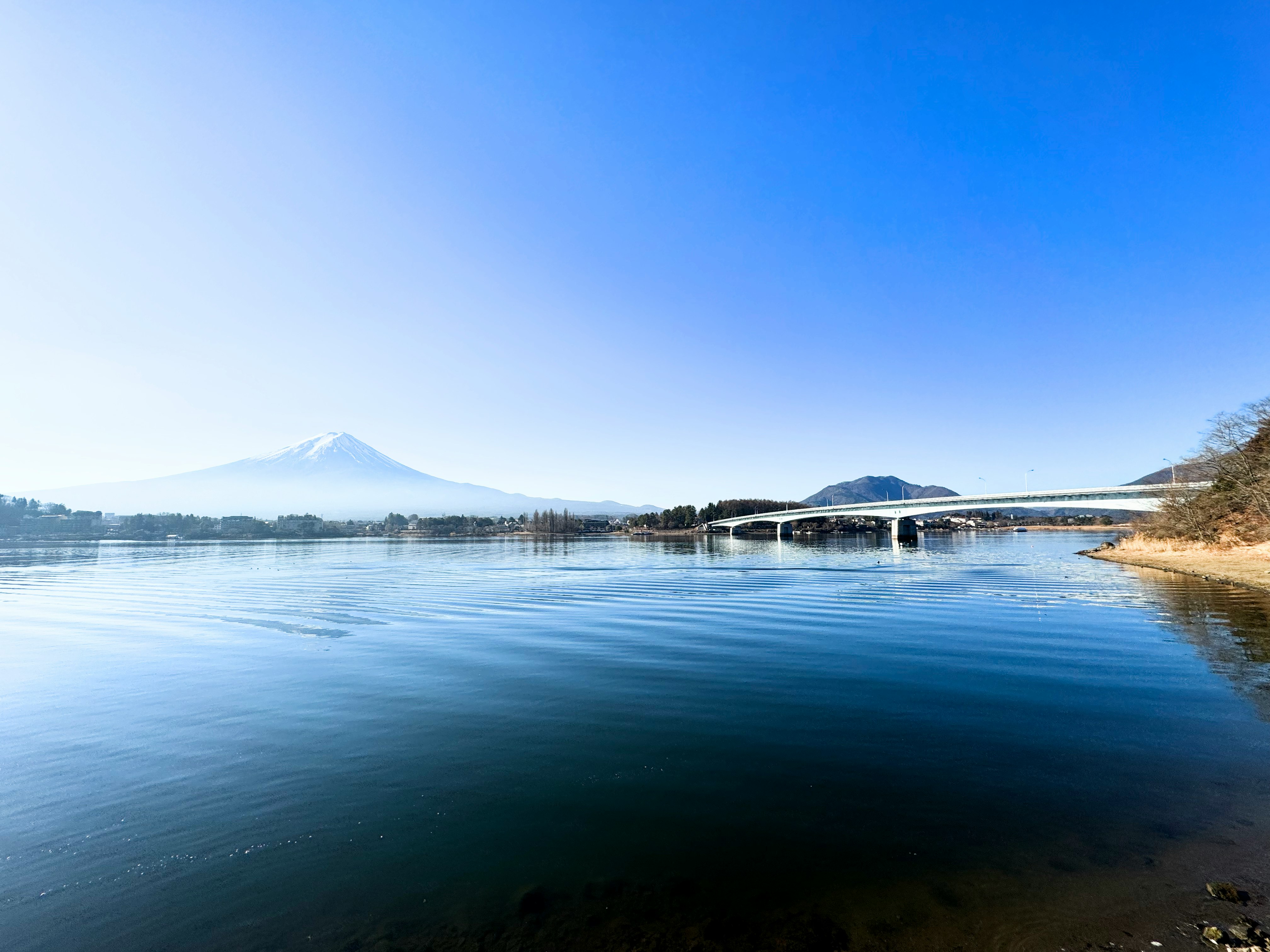 Danau tenang dengan air tenang, pegunungan jauh, dan jembatan