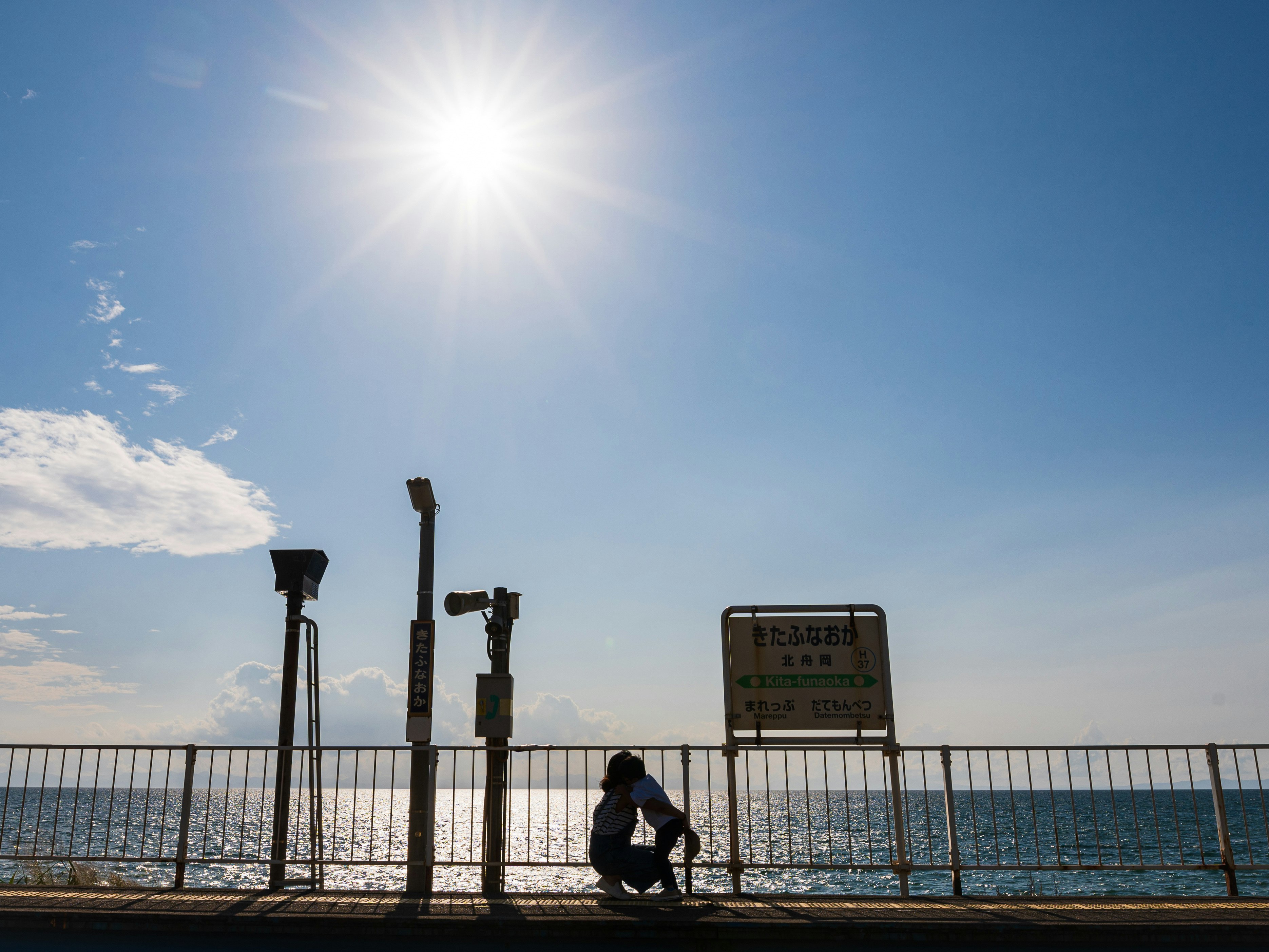 Un enfant court pour enlacer sa mère devant une rambarde en bord de mer