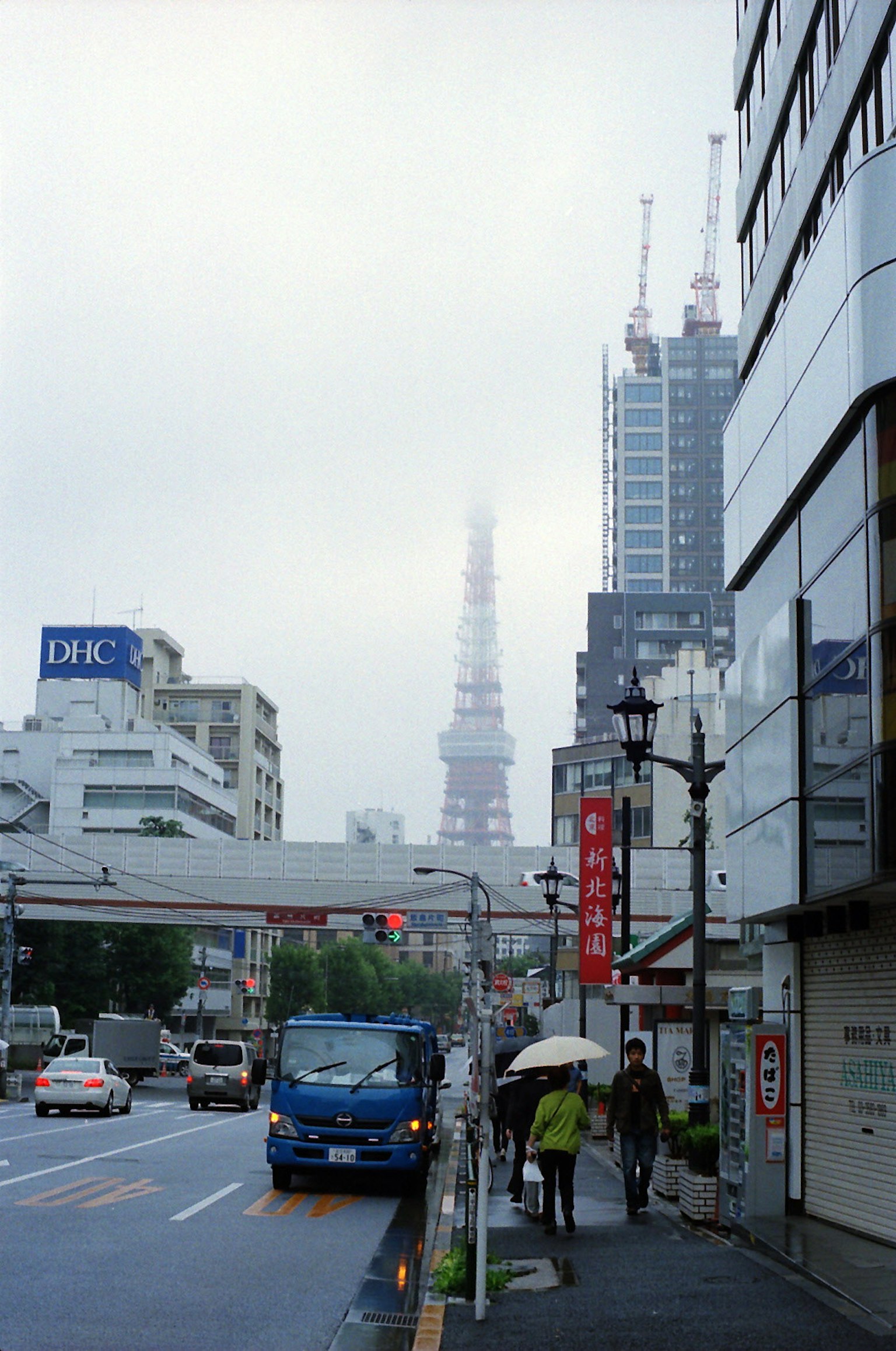 Cảnh thành phố với tháp Tokyo trong sương mù, xe buýt và người đi bộ cầm ô