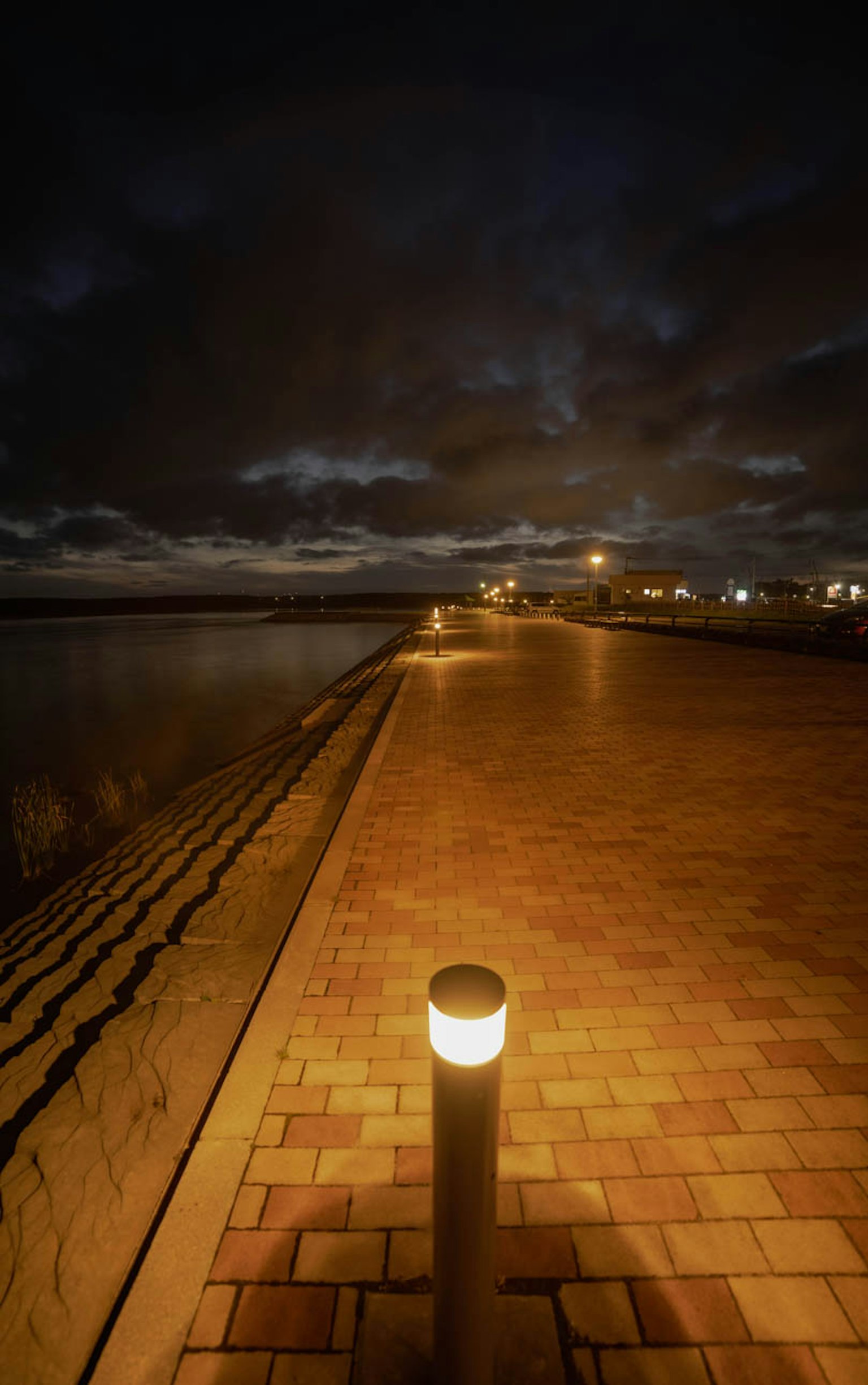 夜晚的海岸鋪裝小道，帶有照明柱和多雲的天空