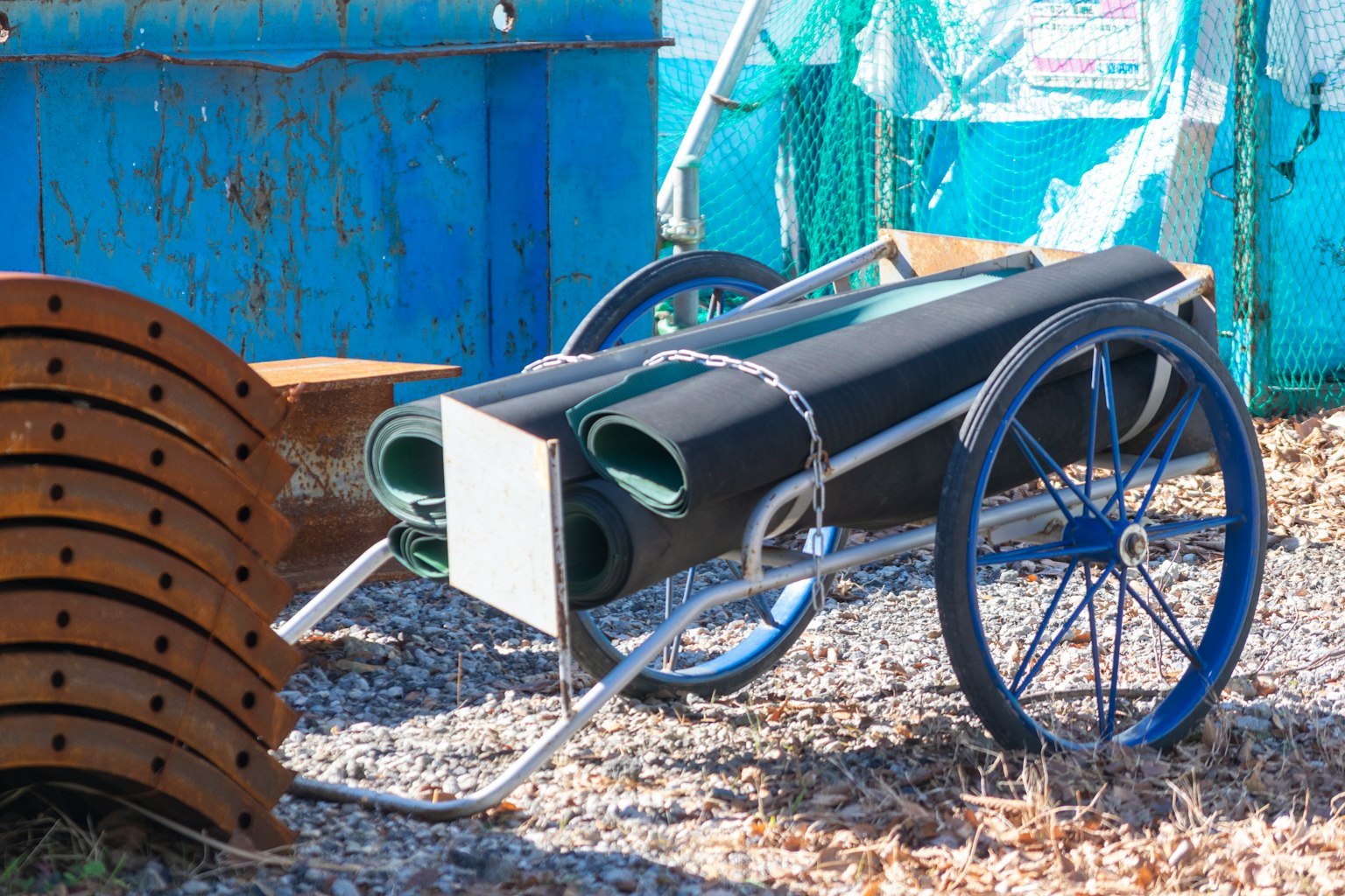 Un chariot avec des tapis noirs enroulés placé contre un fond bleu