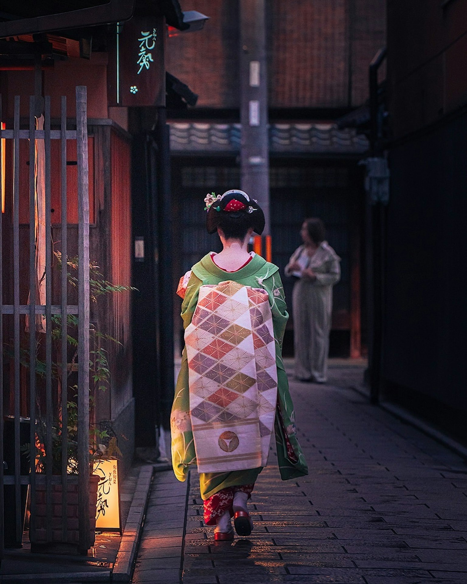 Una mujer en kimono caminando por la noche con otra persona al fondo