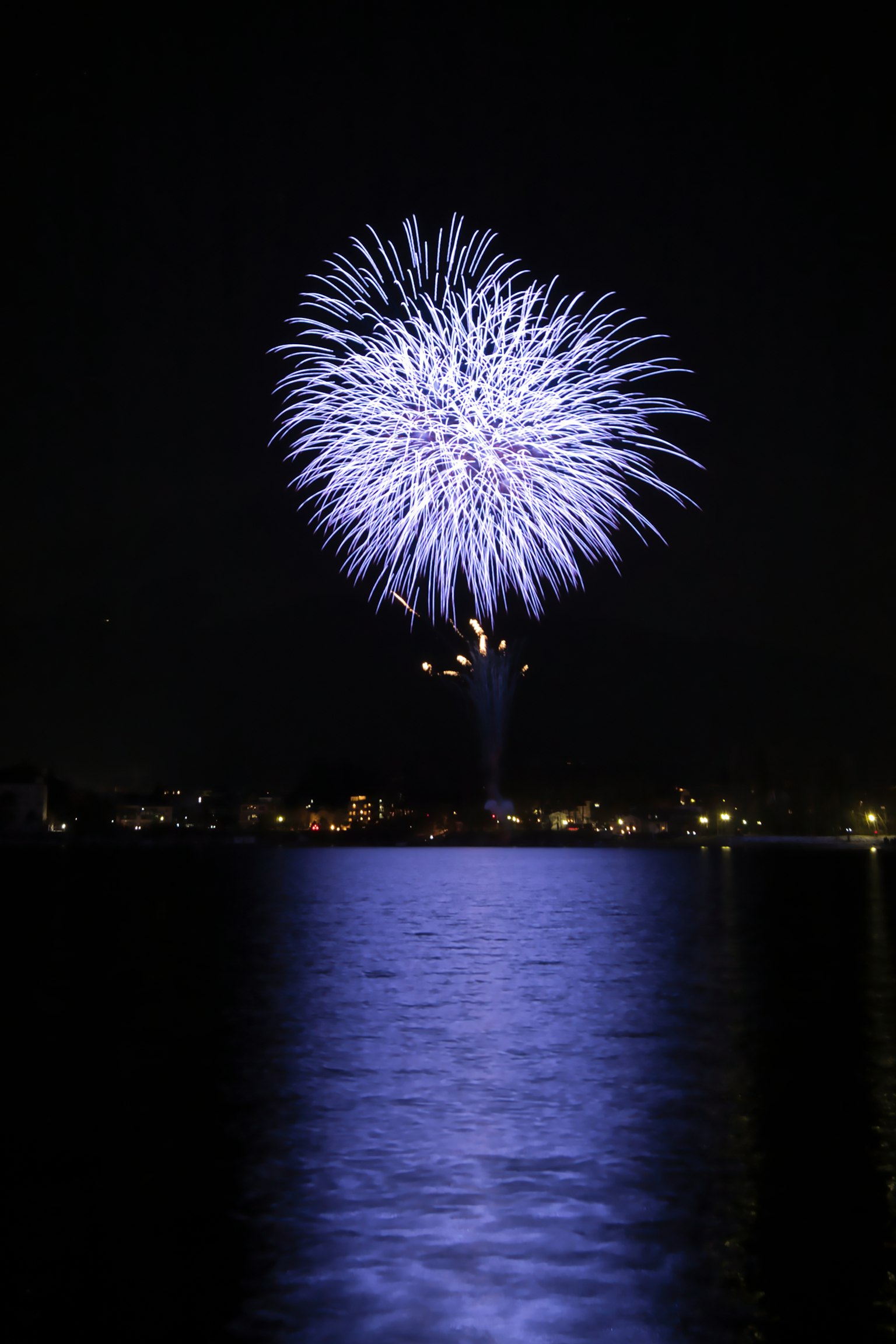 Beautiful scene of purple fireworks blooming in the night sky reflecting on the water