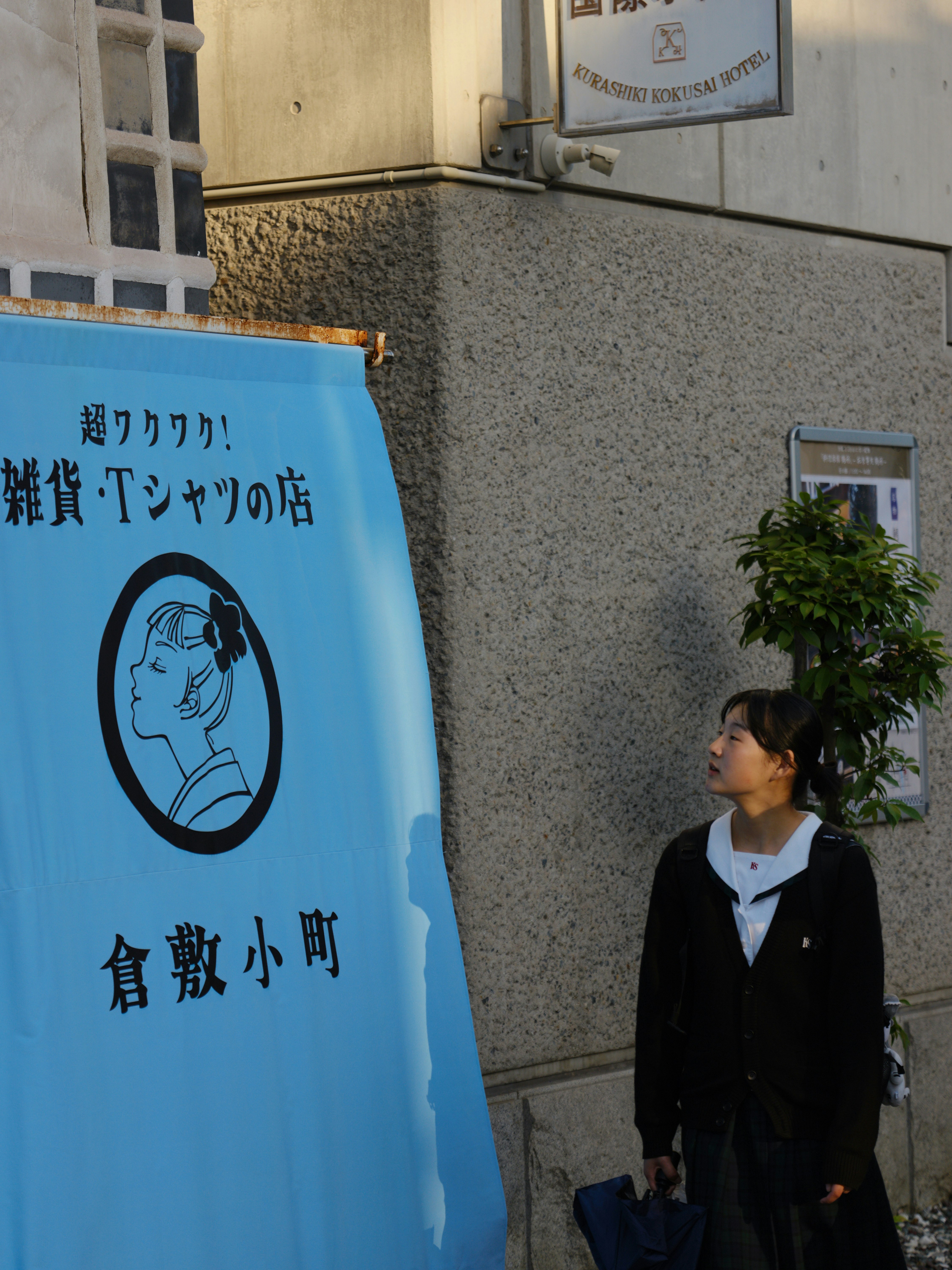 壁の前に立つ人物と青い看板のある路地