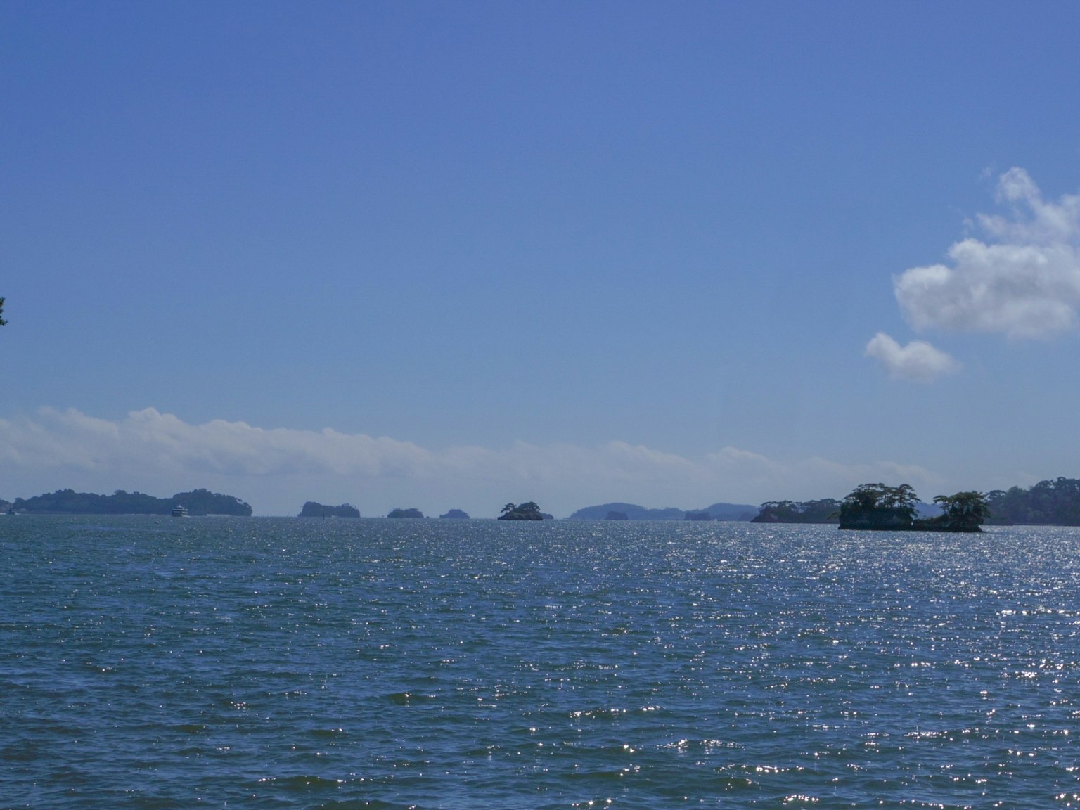ทัศนียภาพที่สวยงามของท้องฟ้าสีฟ้าสดใสเหนือผิวน้ำที่ระยิบระยับพร้อมเรืออยู่ในระยะไกล
