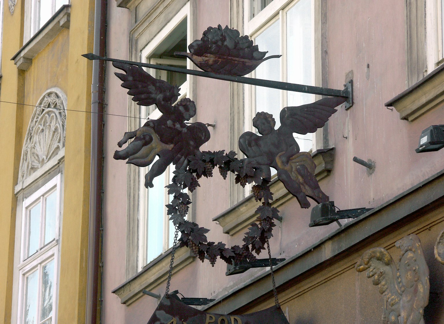 Insegna metallica decorativa montata su un muro con figure di angeli e una corona floreale