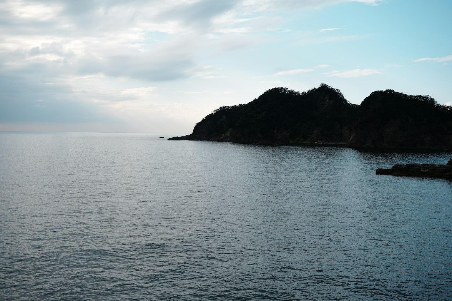Pemandangan laut tenang dengan siluet gunung di kejauhan