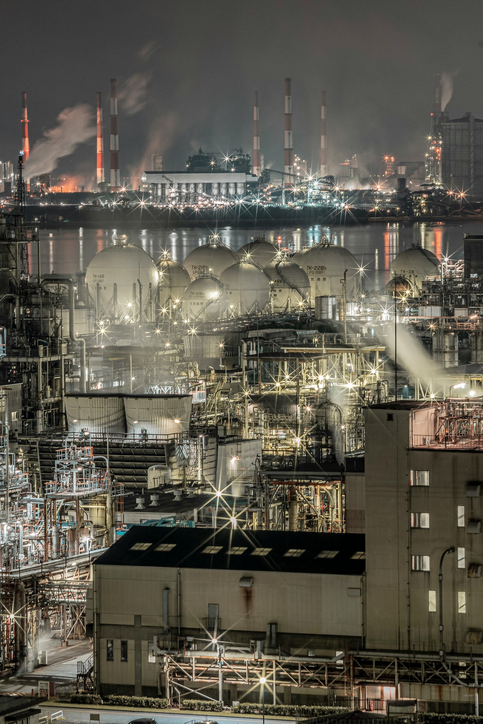 夜间工业景观 featuring tanks and smokestacks with smoke and lights