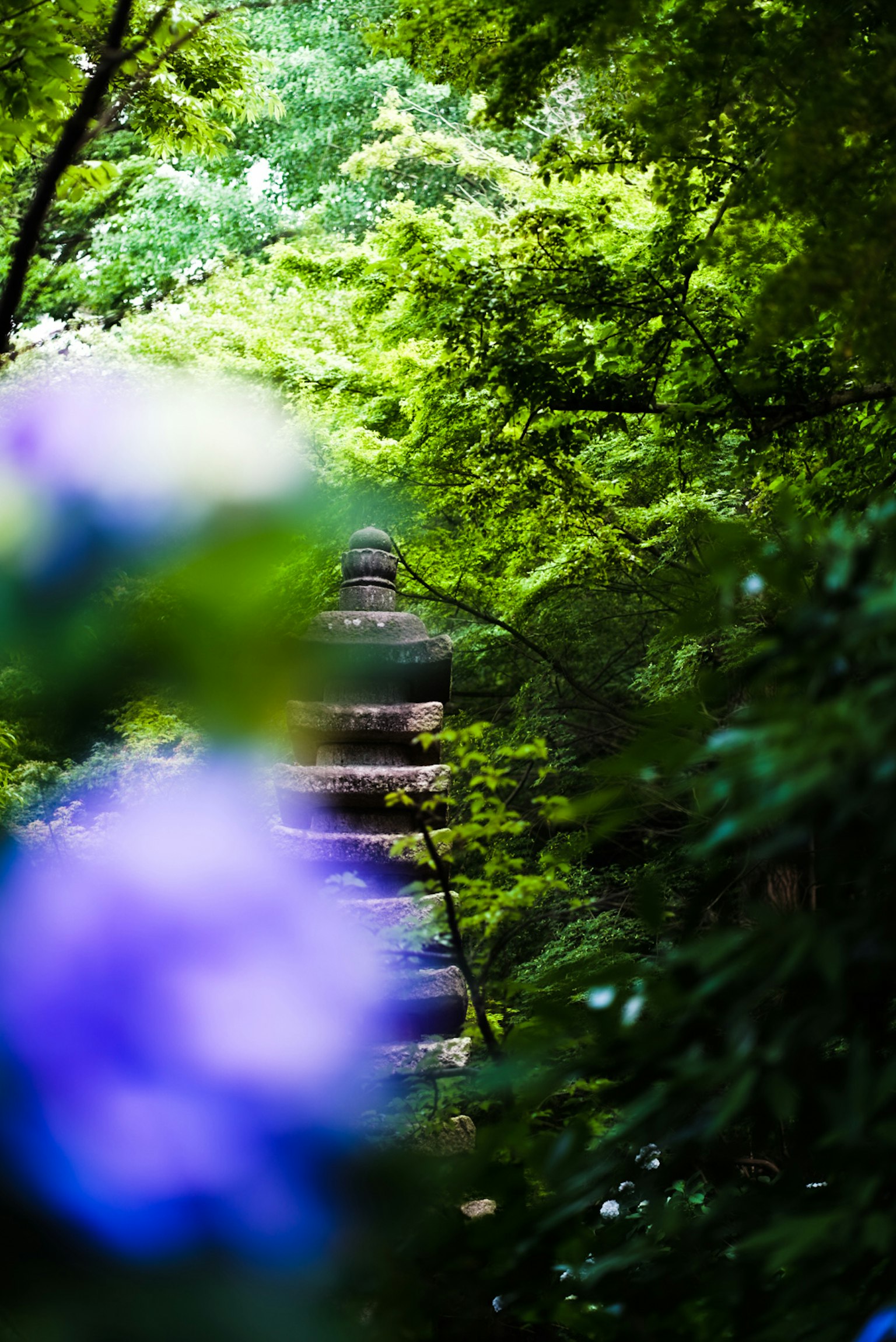 Una vista sfocata di una pagoda in pietra circondata da un fogliame verde lussureggiante e fiori viola