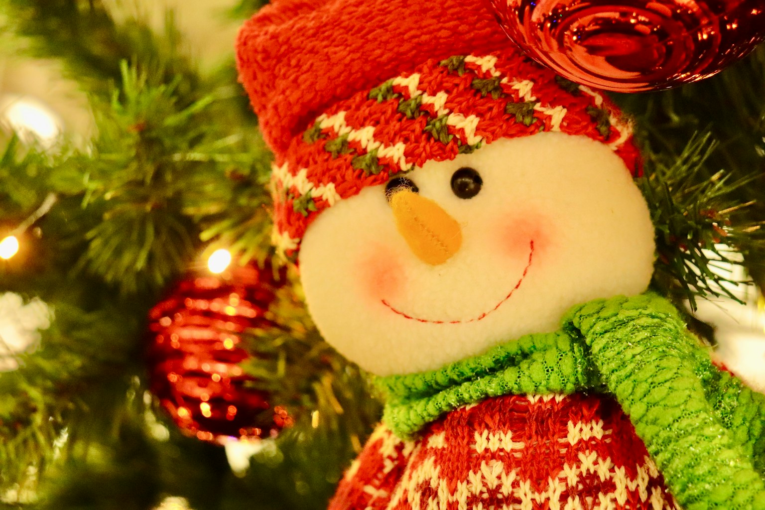 Smiling snowman ornament near a Christmas tree