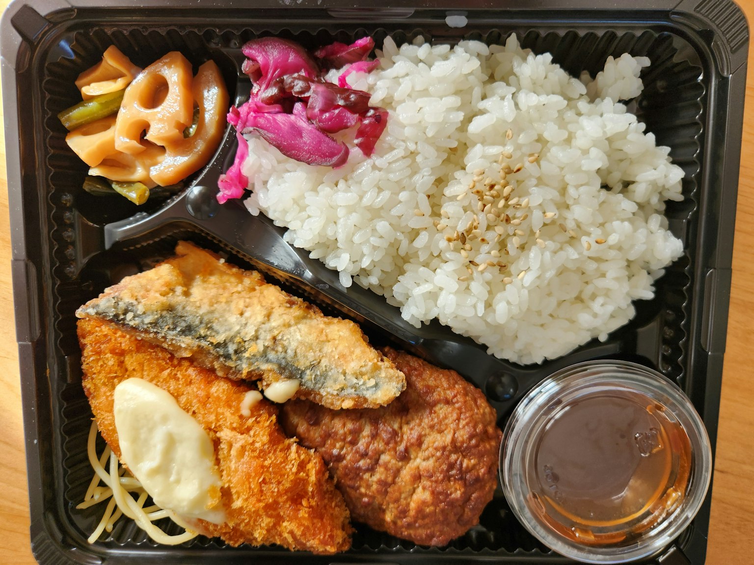 一个便当盒，里面有炸鱼、米饭、腌制蔬菜和蘸酱