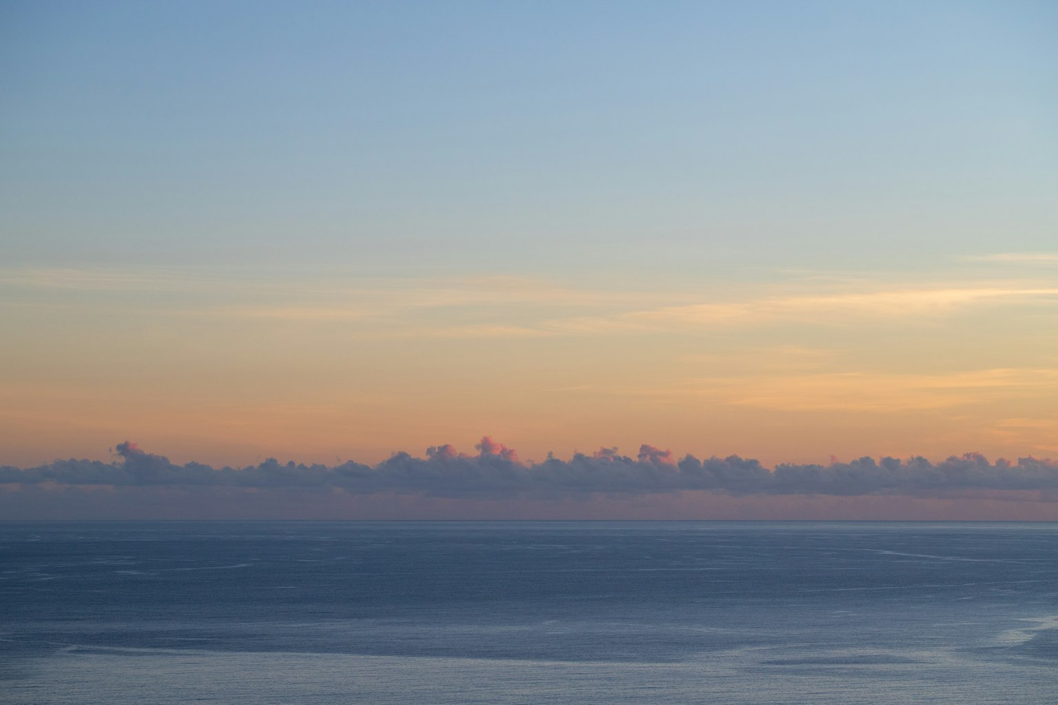 Vue panoramique d'une mer calme sous un ciel pastel avec des nuages orange