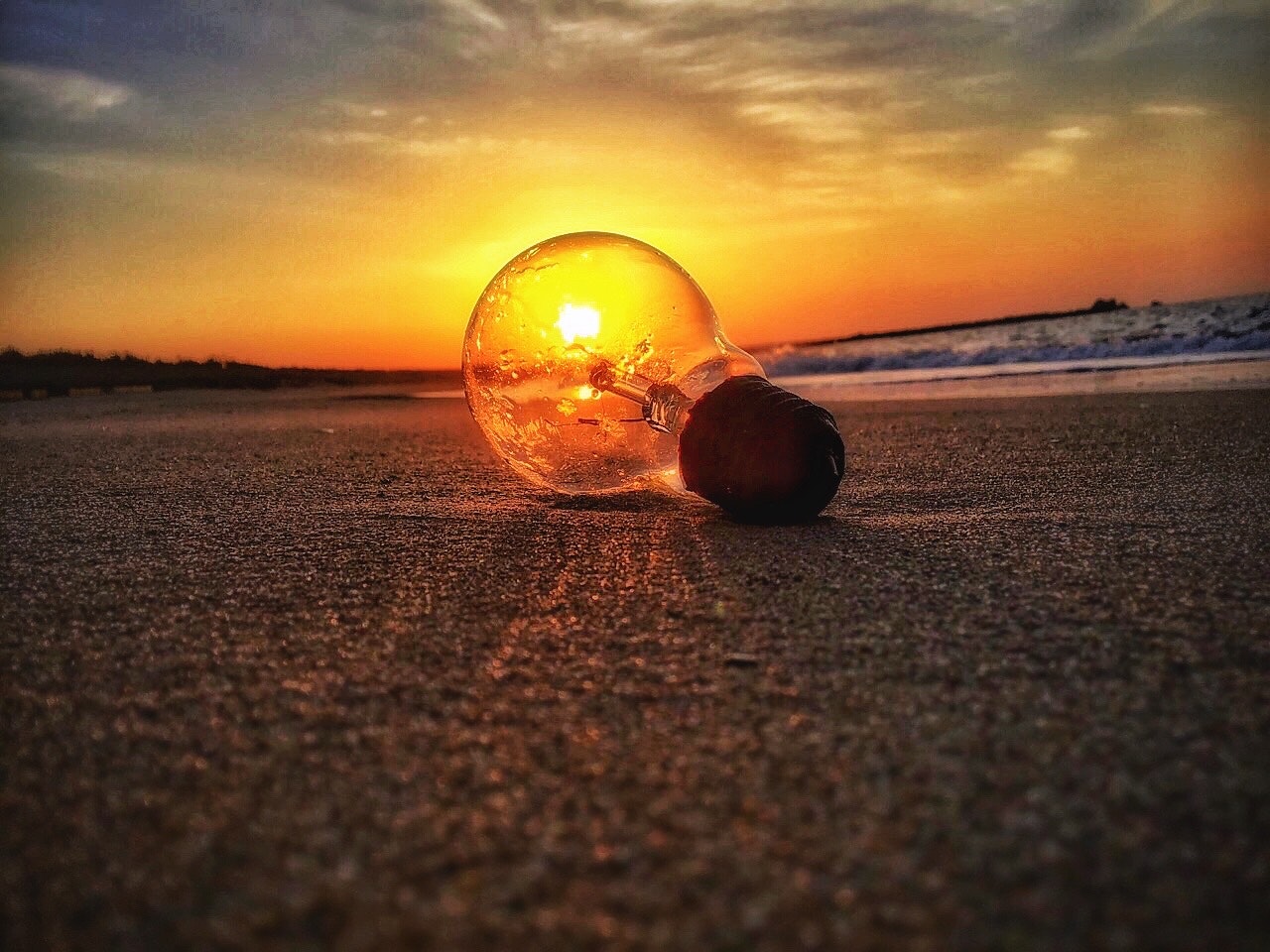 夕陽の砂浜に転がる光る電球の漂着物
