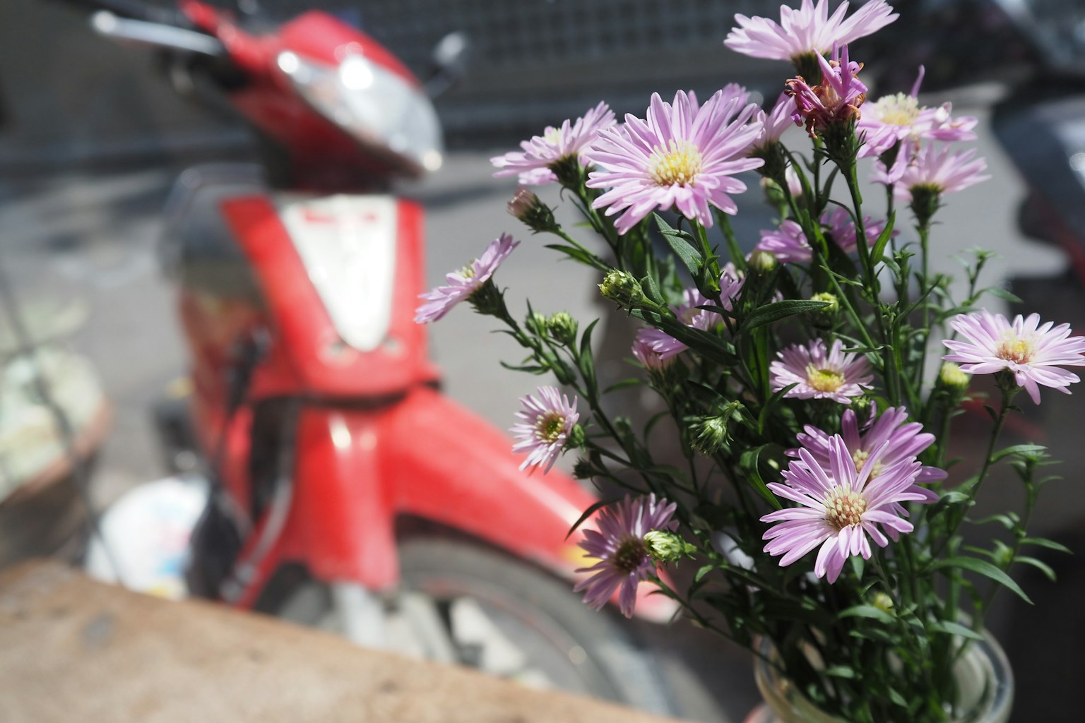 Ein Strauß lila Blumen vor einem roten Roller