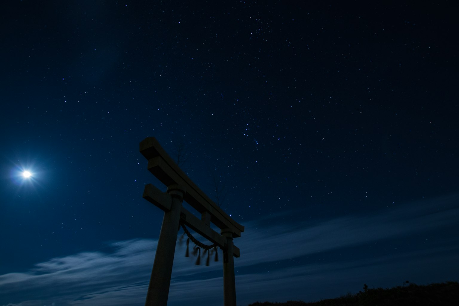 Torii-Tor silhouettiert vor einem sternenreichen Nachthimmel mit einem hellen Mond