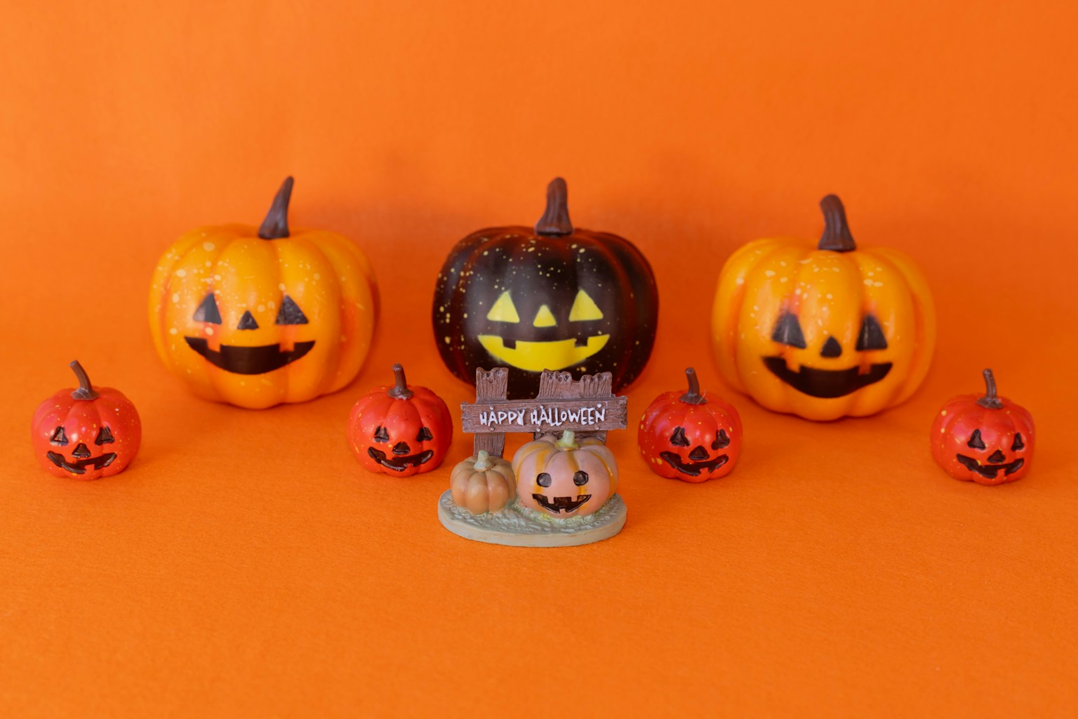 Labu Halloween dengan wajah tersenyum di latar belakang oranye menampilkan labu besar dan kecil