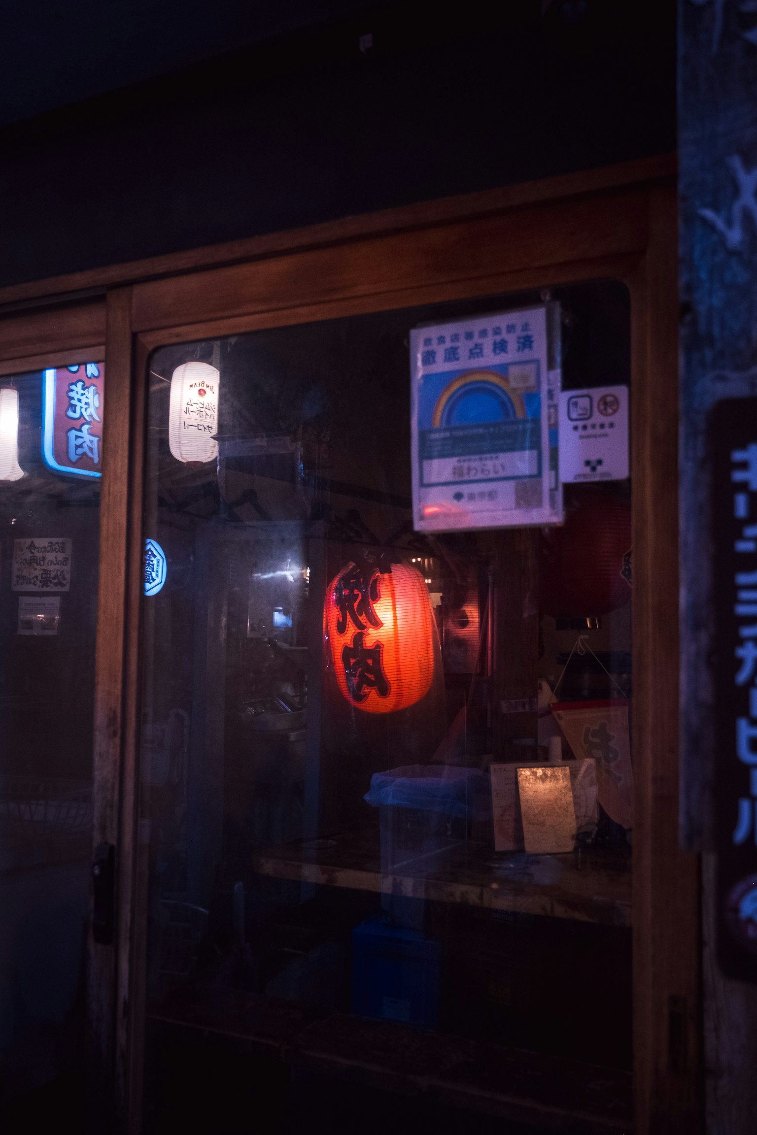 Traditional Japanese shop at night featuring a bright red lantern and various signs