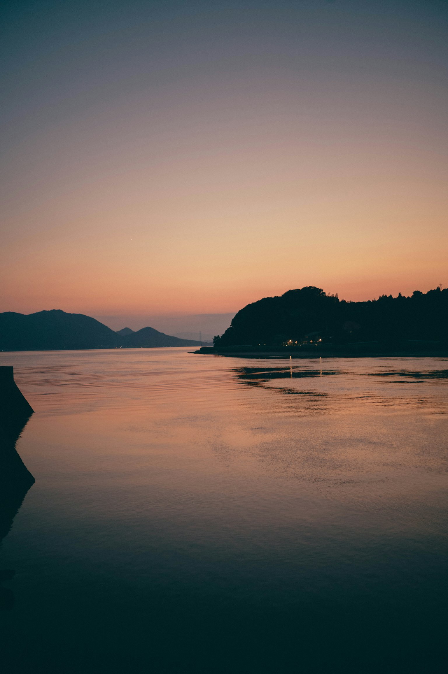 Tramonto sereno su acque tranquille che riflettono montagne e tonalità morbide