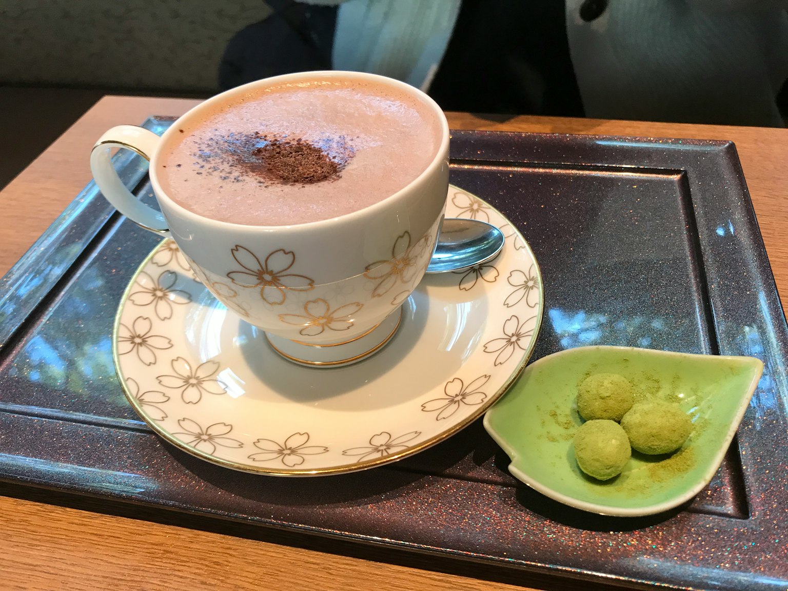 Sô cô la nóng trong cốc trắng có hoa văn và bánh ngọt matcha trên đĩa xanh