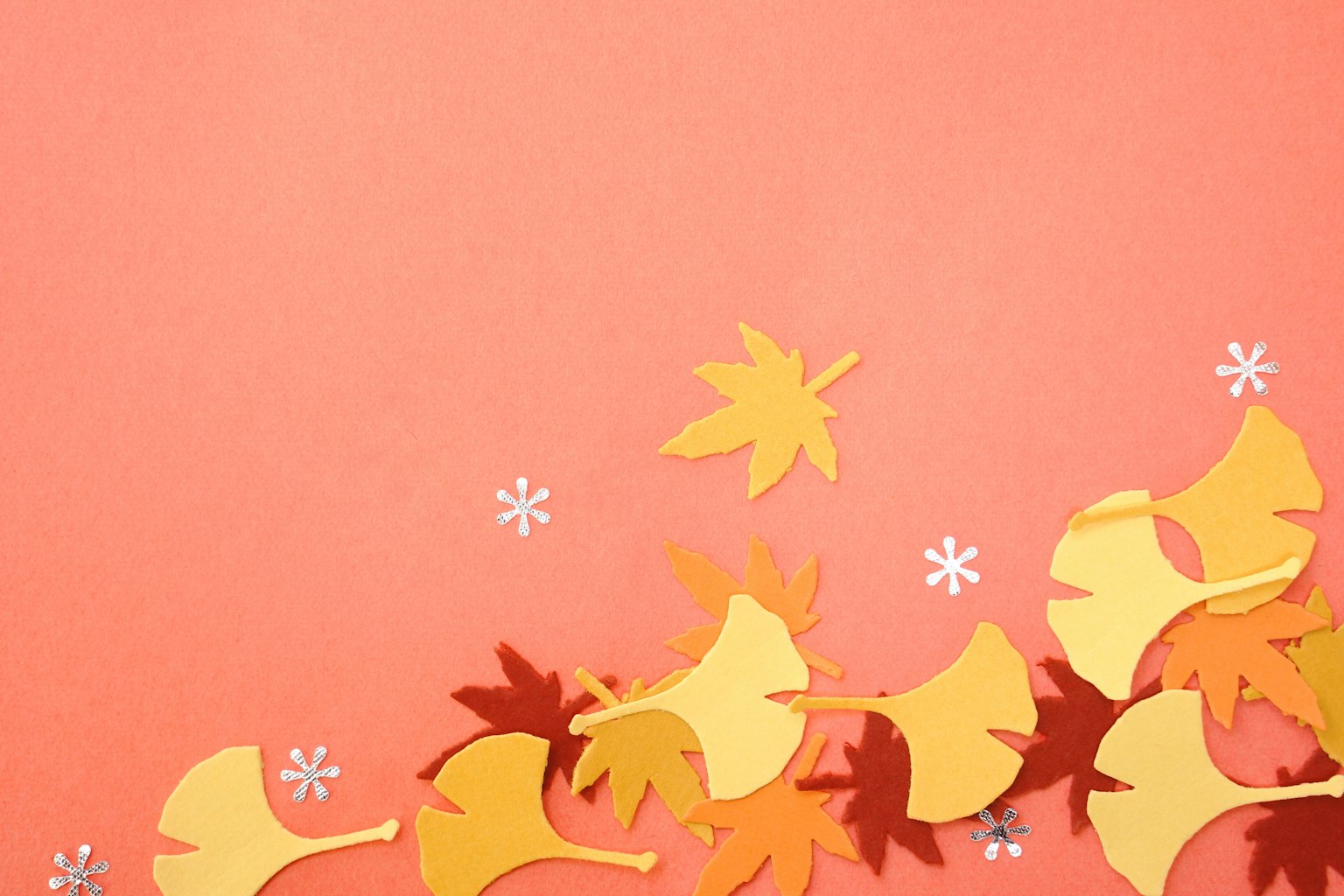 Feuilles en papier colorées jaunes et oranges éparpillées sur un fond rose