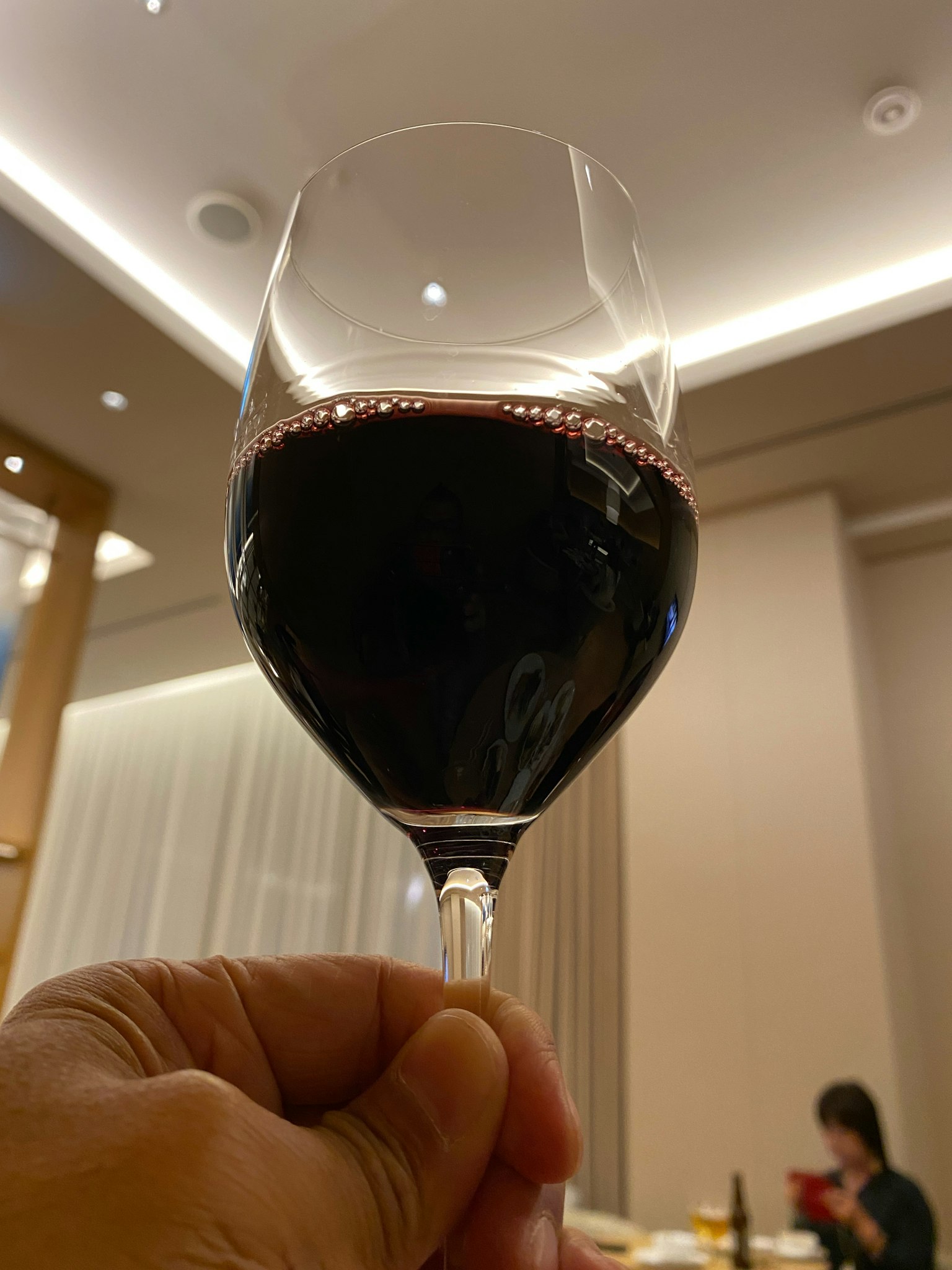 Mano sosteniendo una copa de vino tinto con iluminación interior al fondo